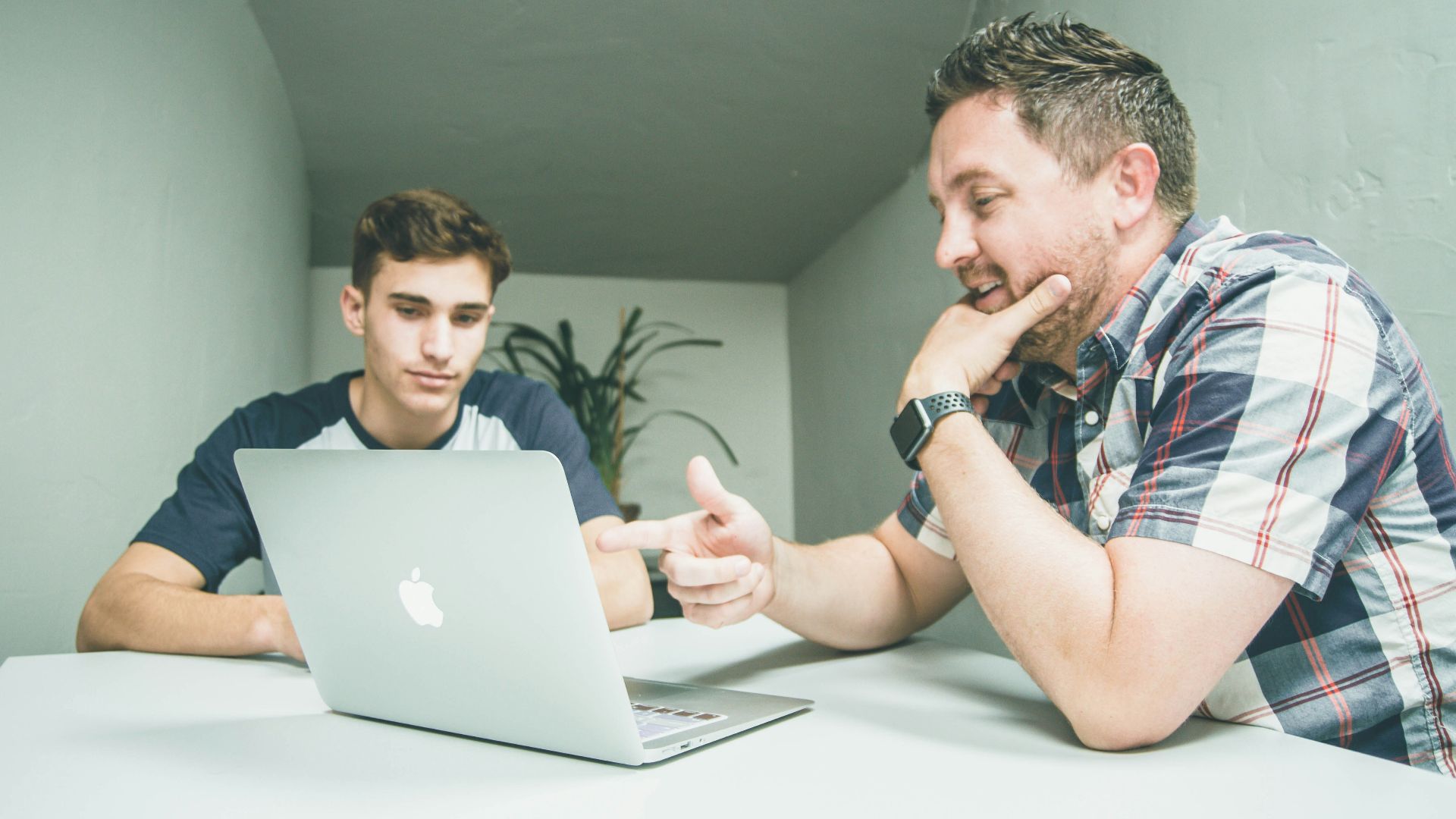 man wearing white and black plaid button-up sports shirt pointing the silver MacBook