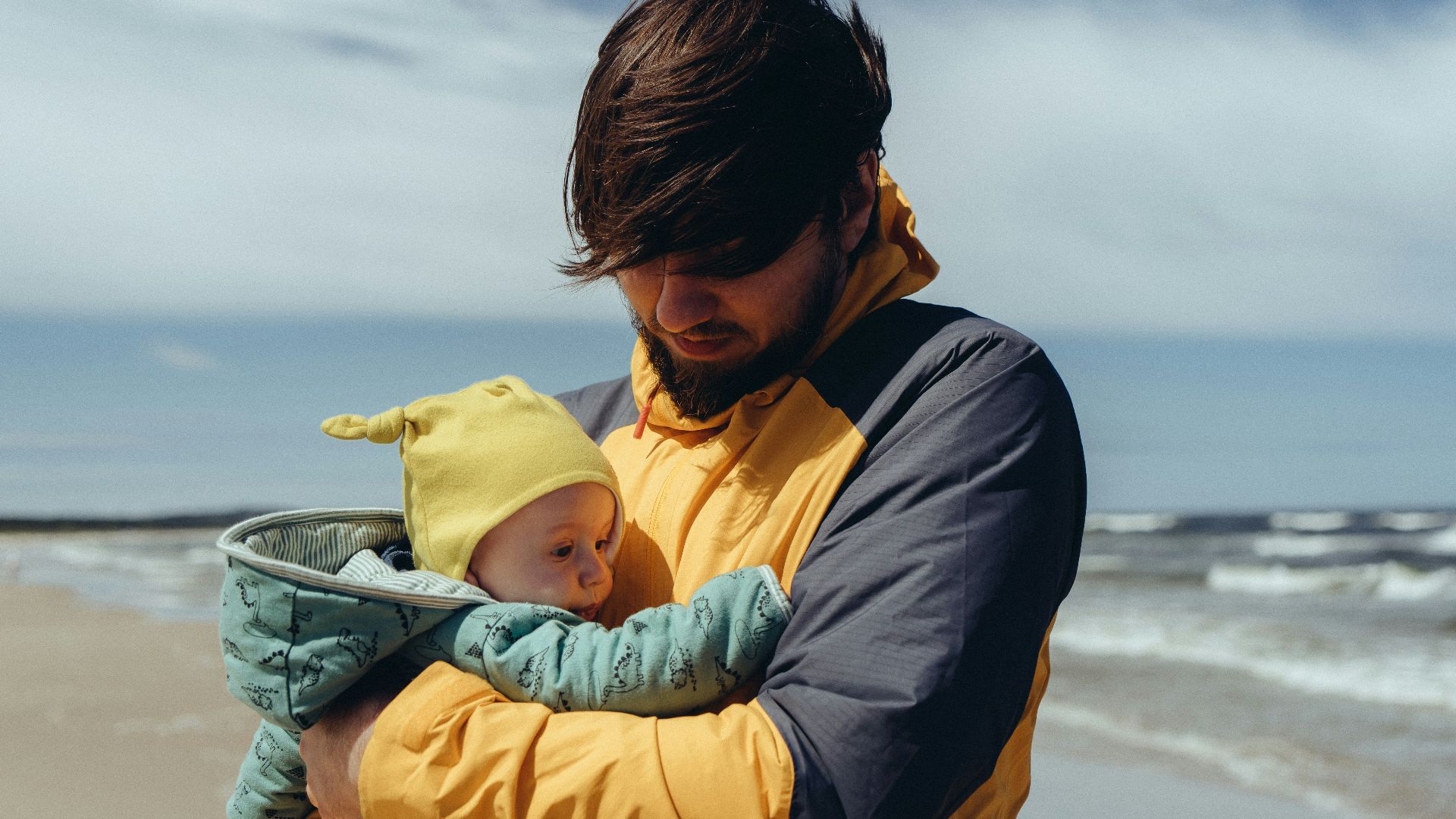 man in black jacket carrying baby in yellow hoodie