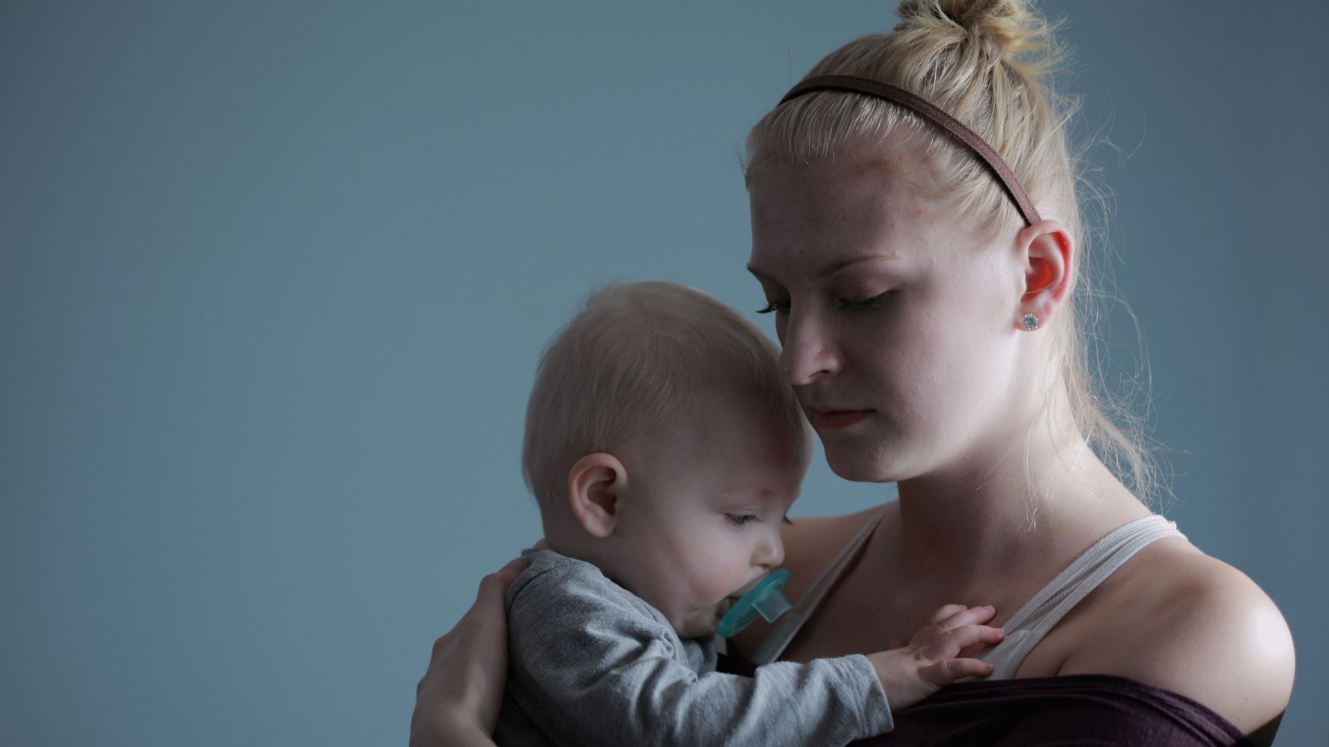 woman carrying baby with pacifier in mouth