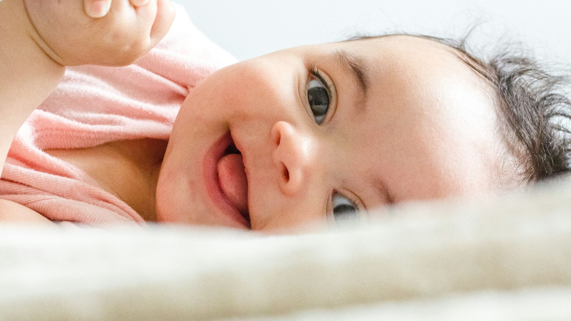 baby in pink shirt lying on white textile