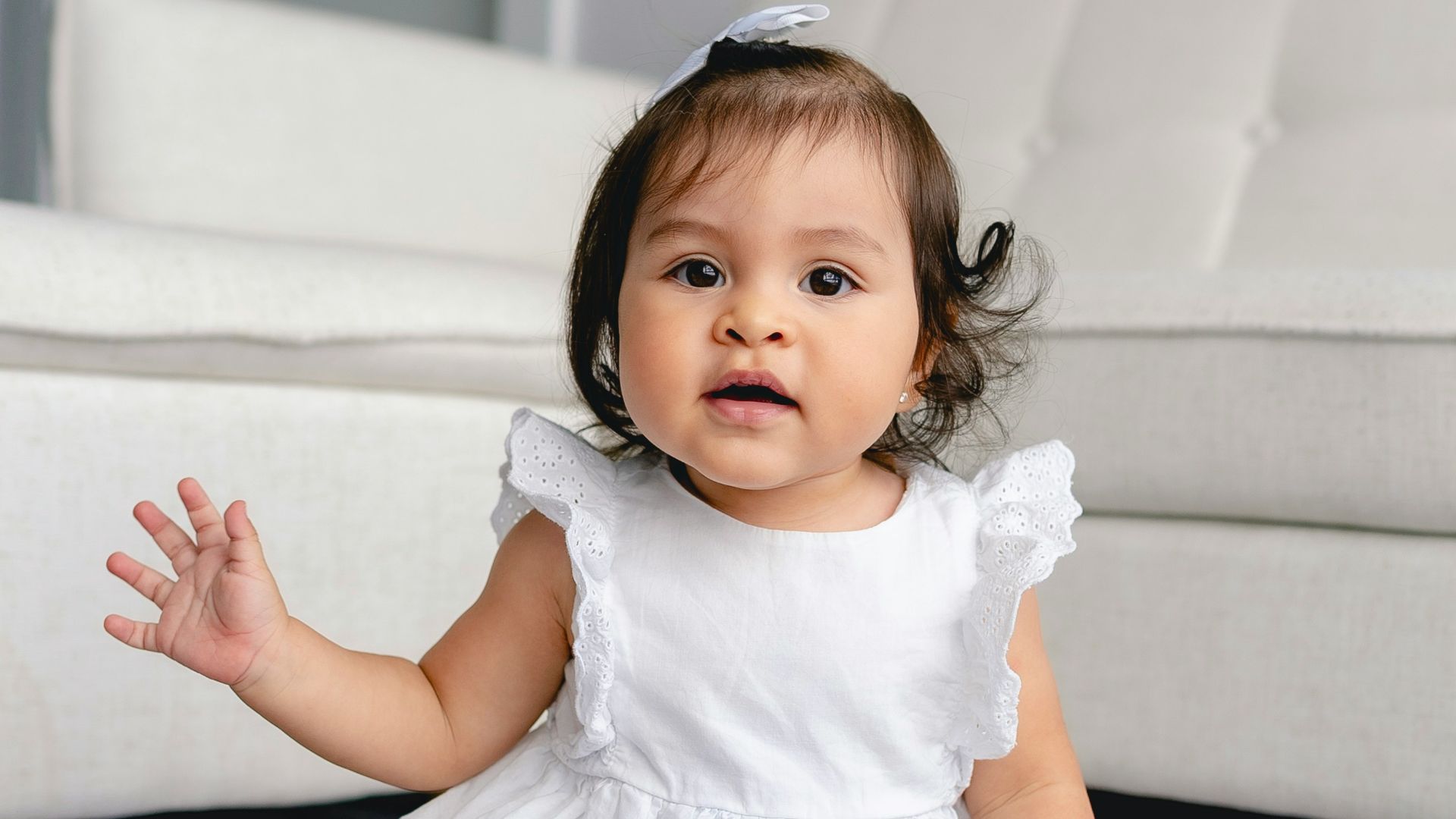 toddler wearing white dress sitting beside white sofa