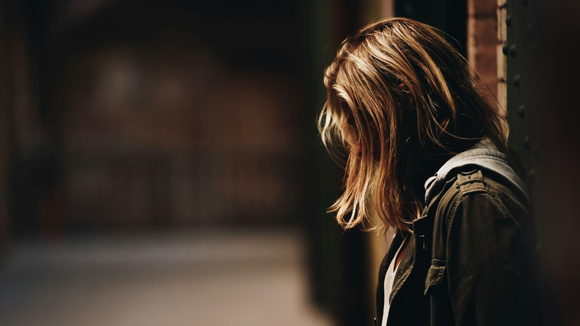 woman leaning against a wall in dim hallway