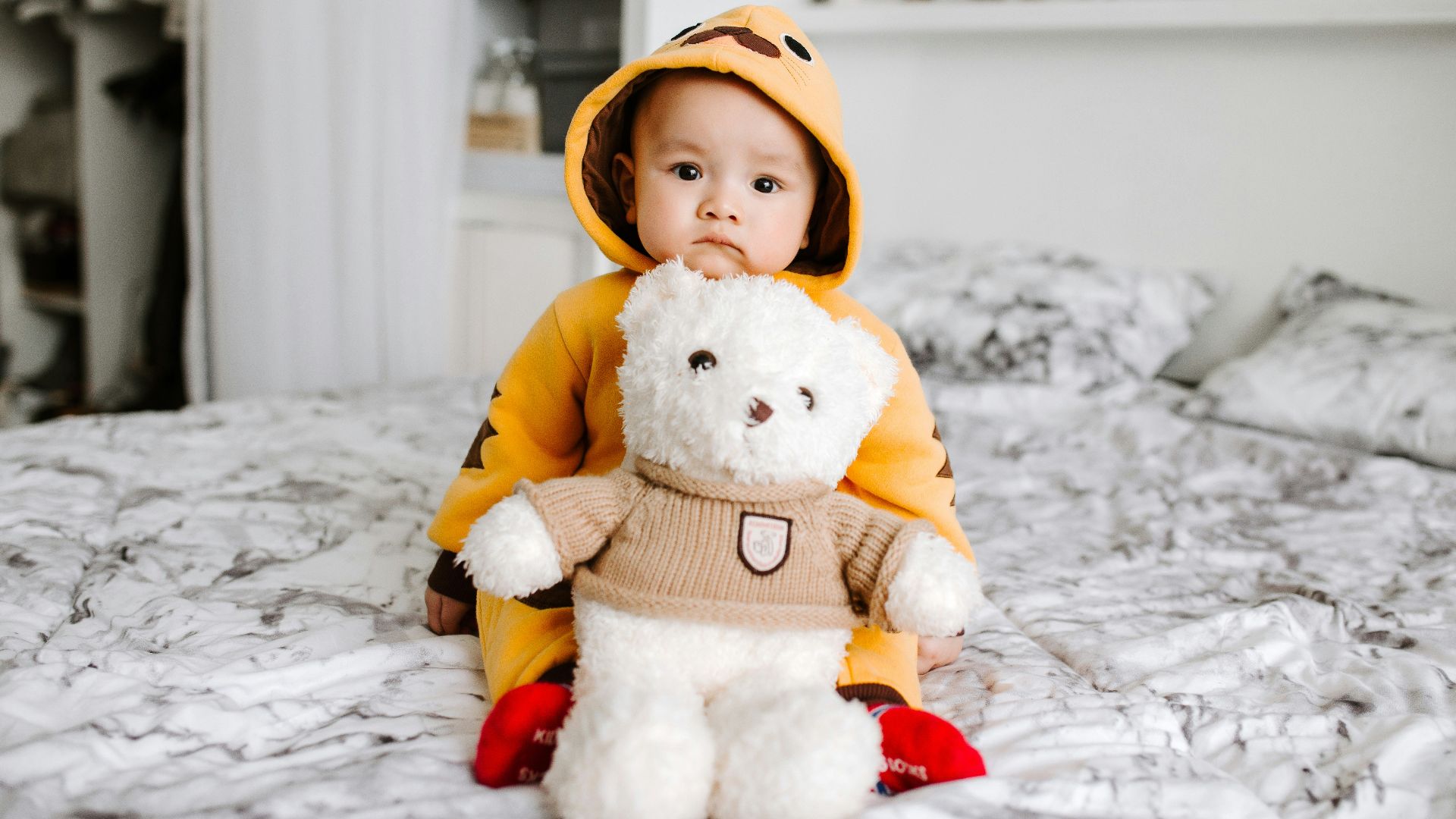 toddler sitting on bed beside white bear plush toy