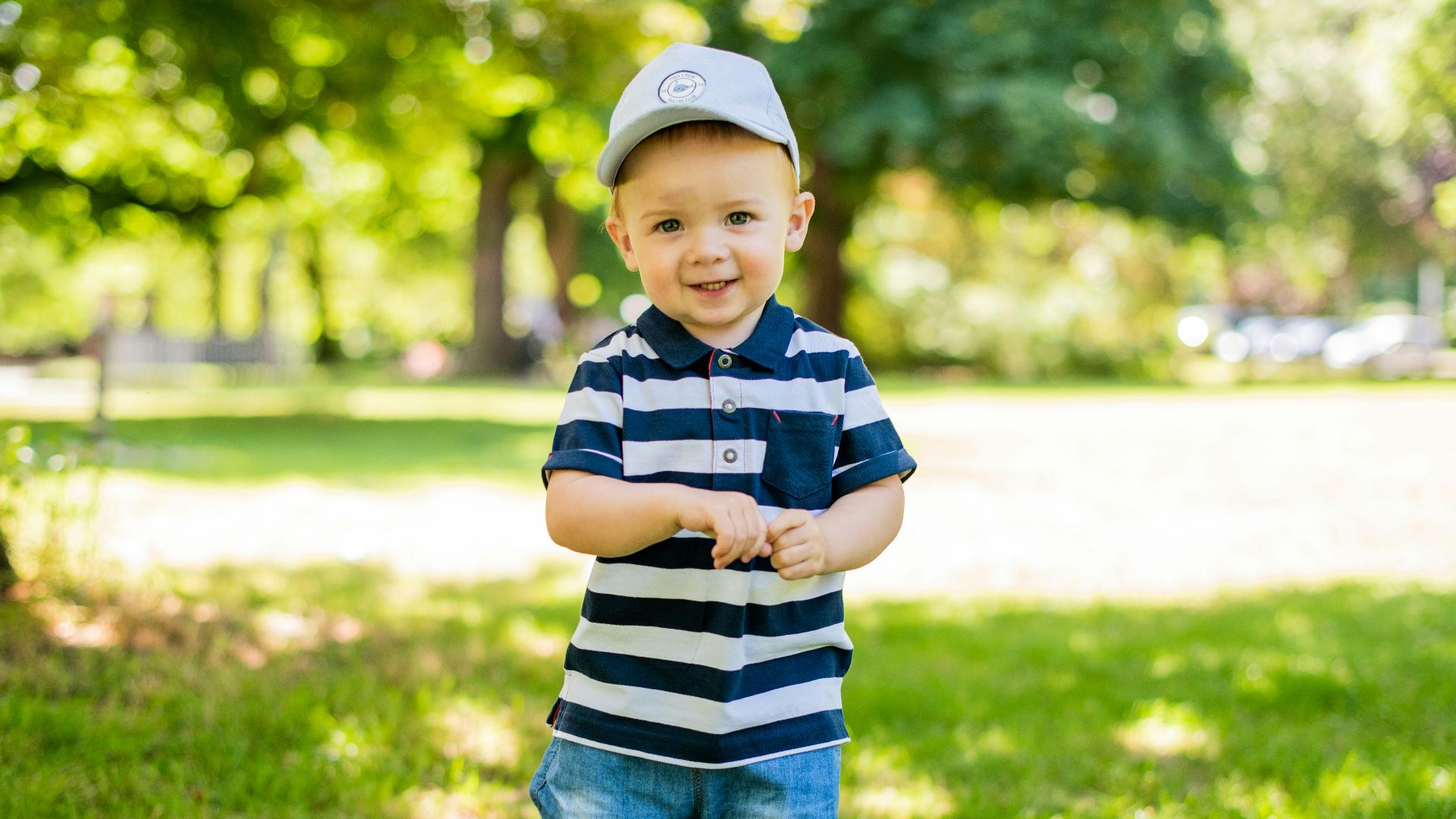 boy in black and white stripe polo shirt and blue denim shorts standing on green grass