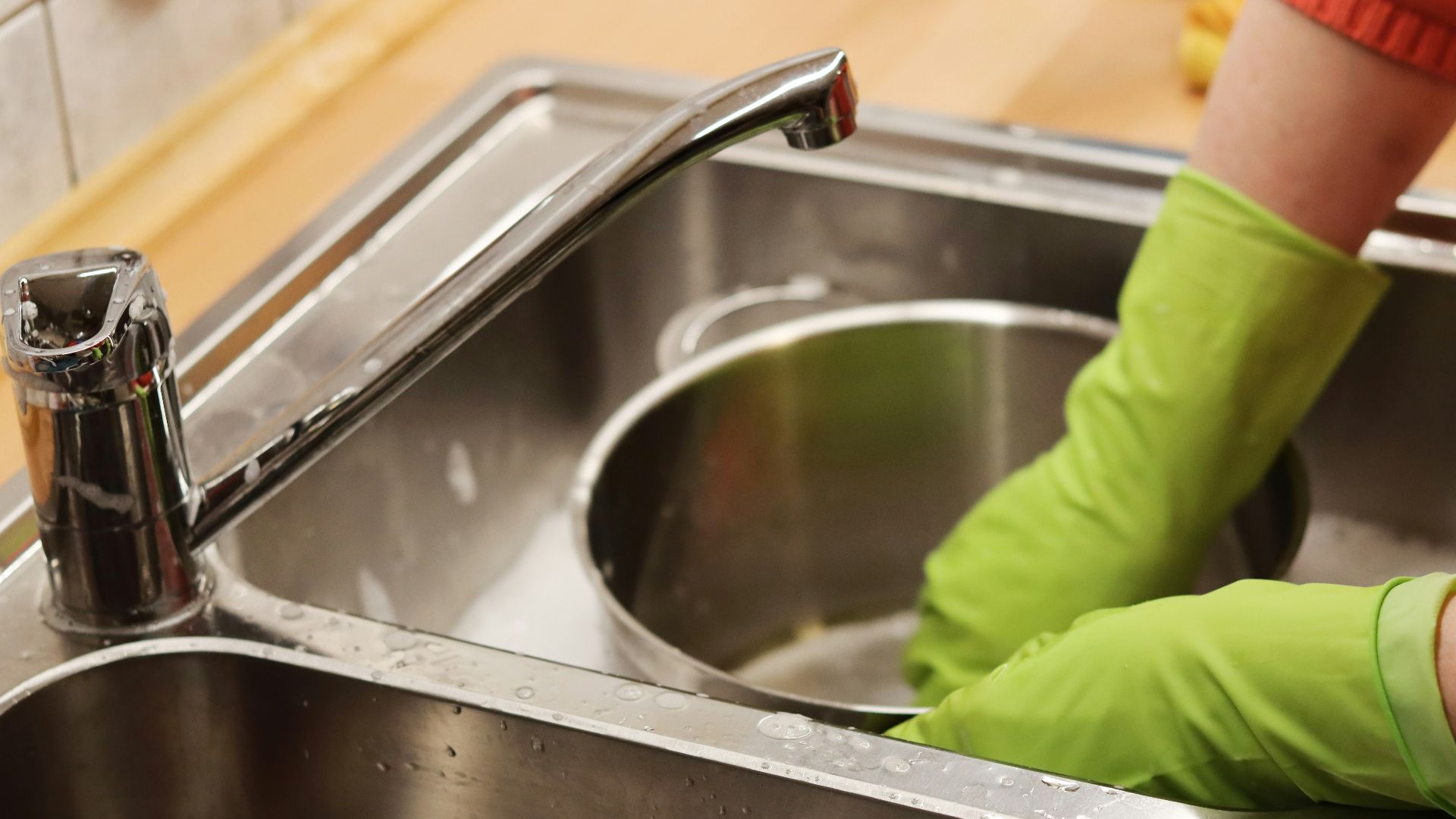 person in green long sleeve shirt washing stainless steel sink