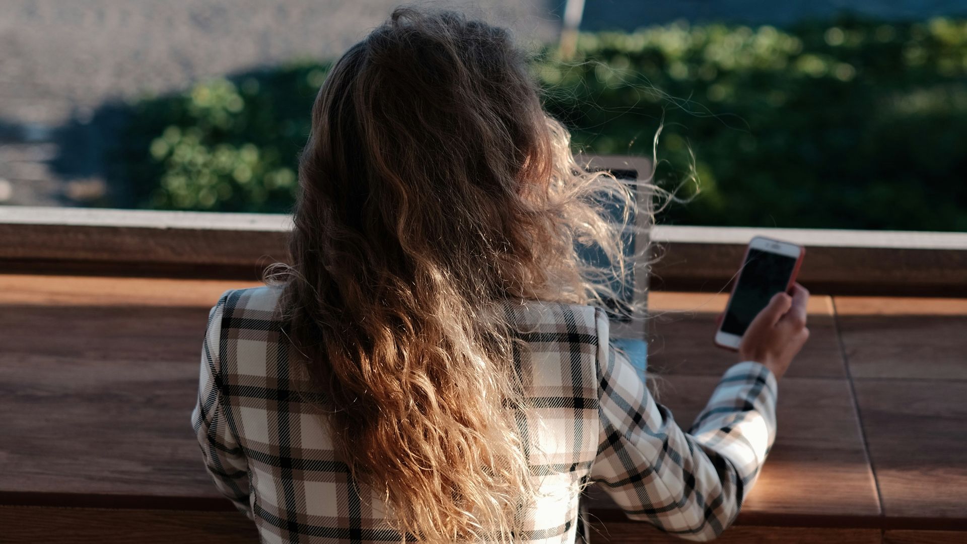 woman in white and black plaid shirt holding black smartphone