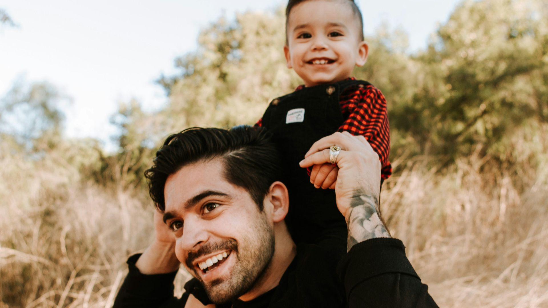 man in black jacket carrying baby in red and white checkered shirt during daytime