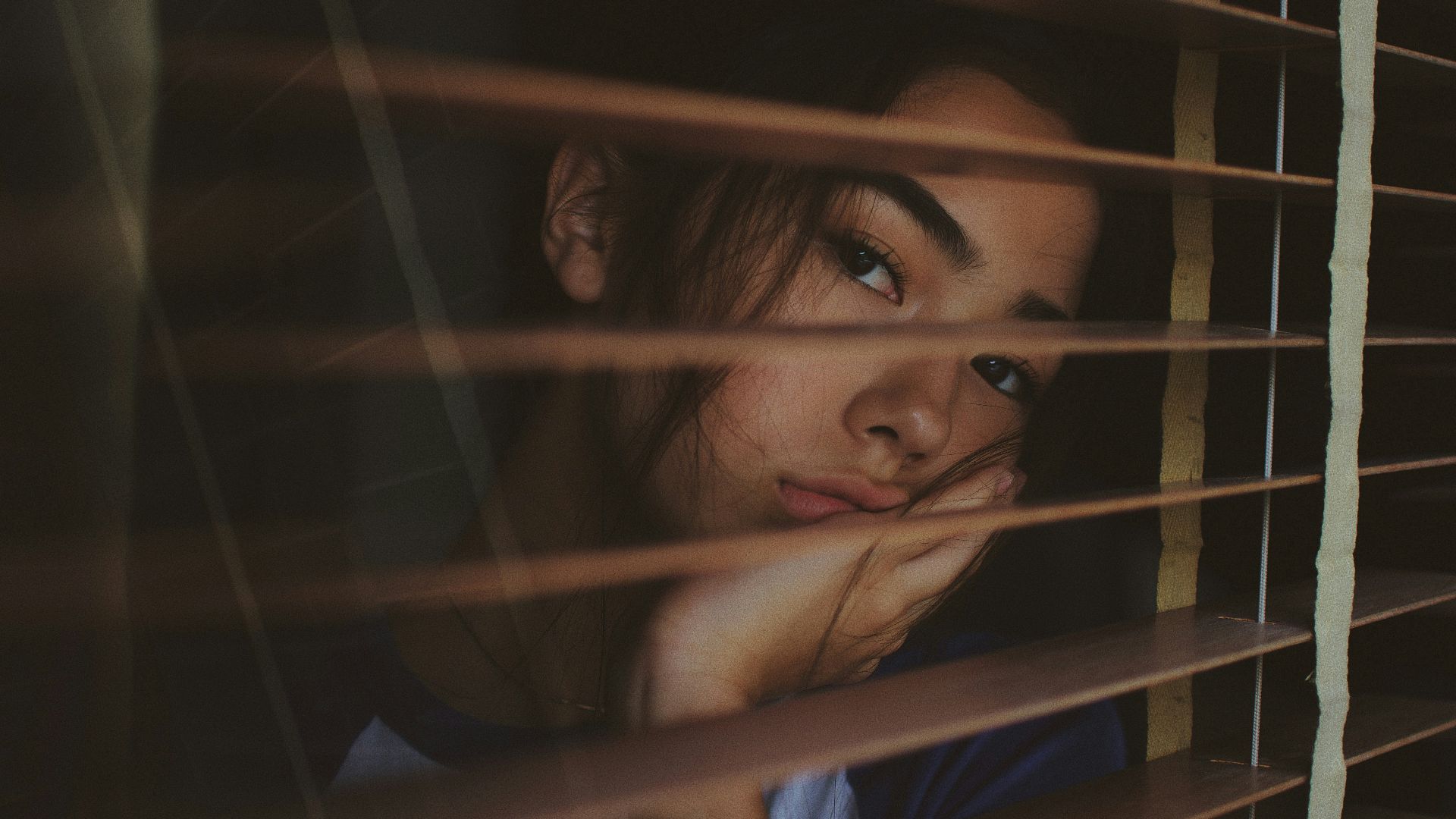 a woman looking out of a window with blinds