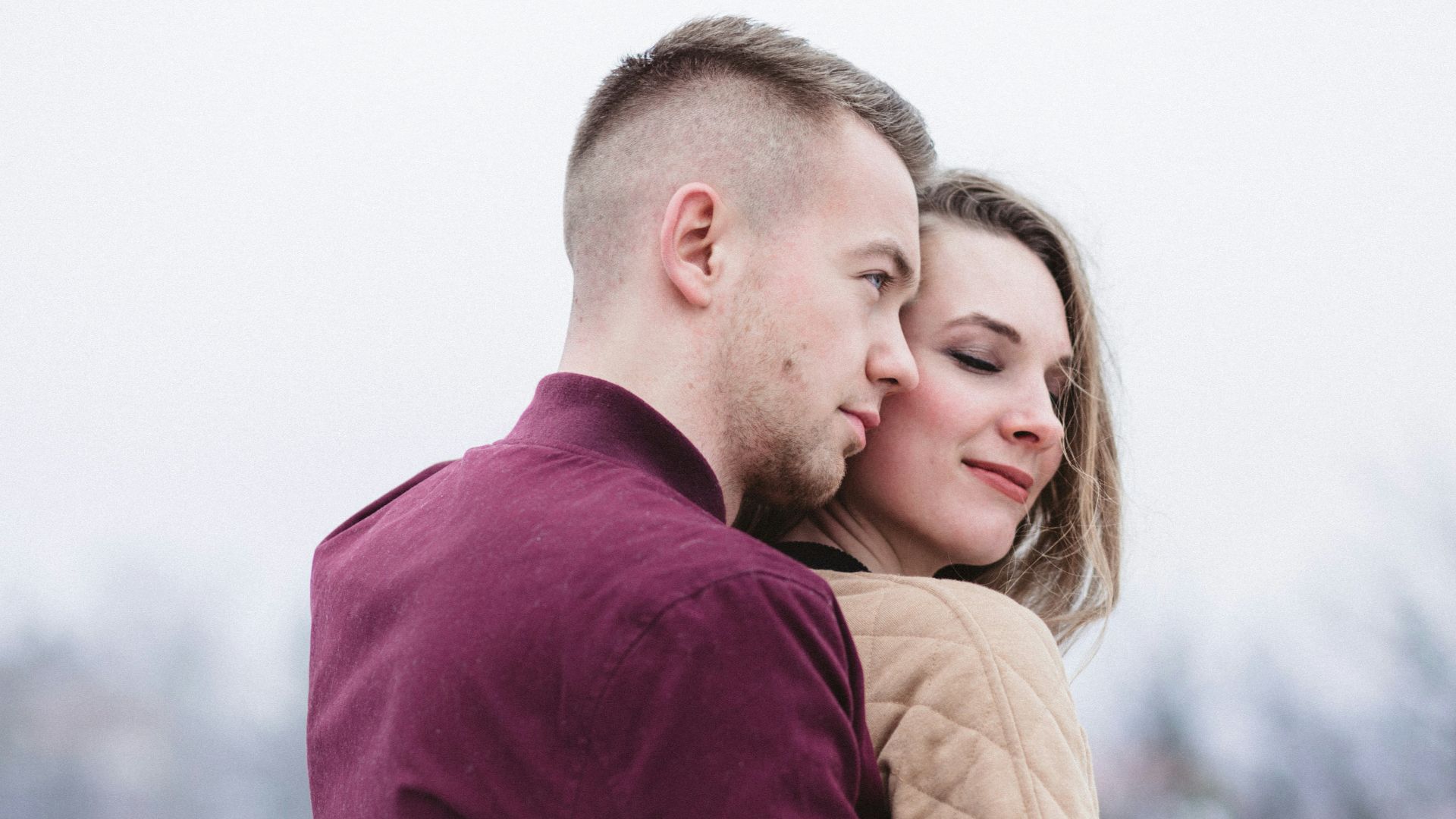man hugging woman while standing on snowy weather