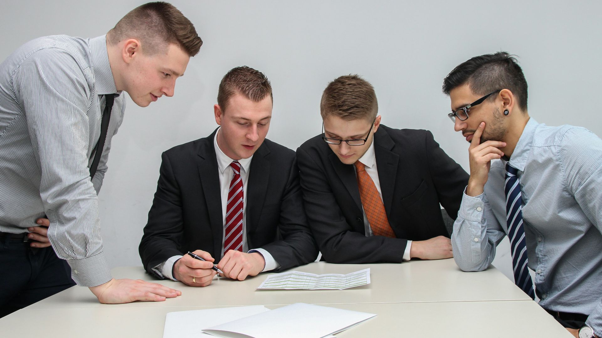 four men looking to the paper on table