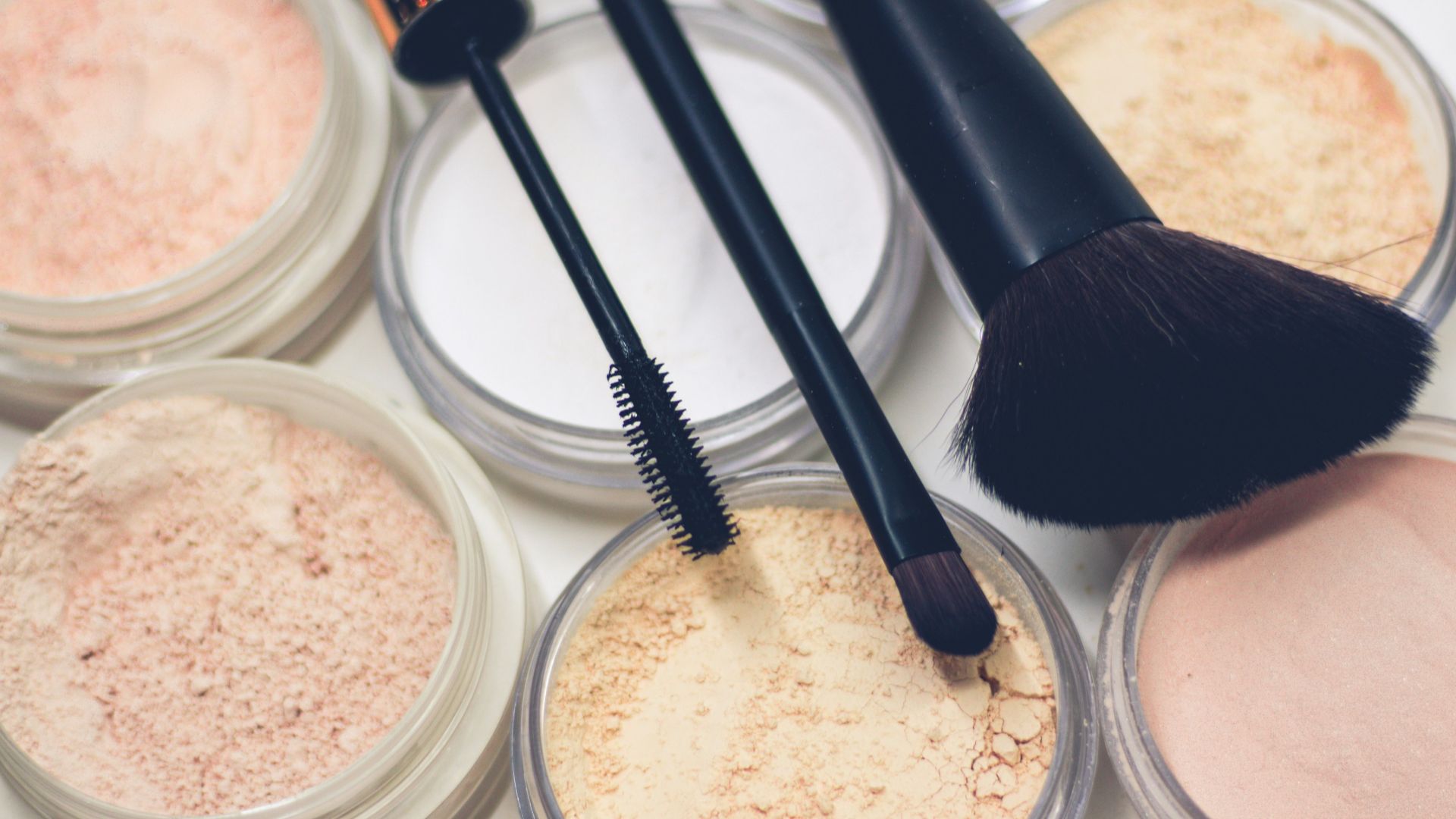 three makeup brushes on top of compact powders