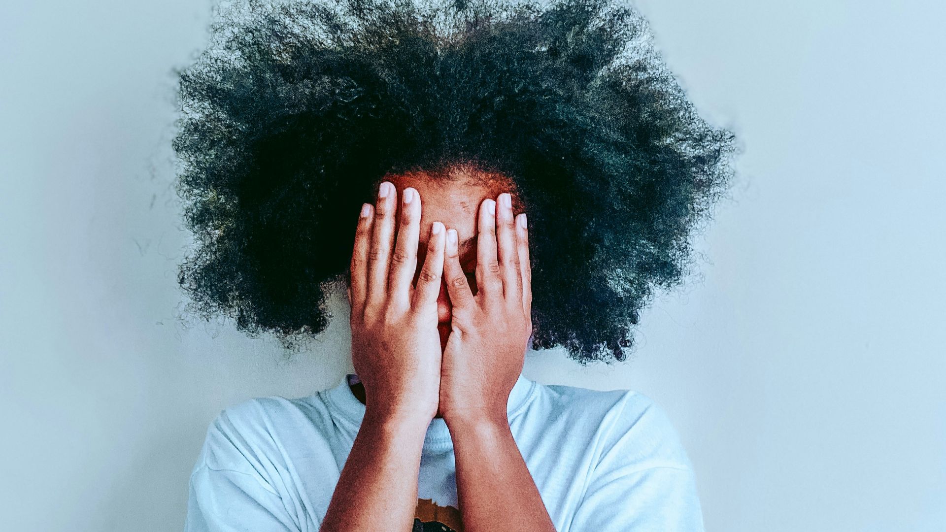 man in white t-shirt covering his face with his hair