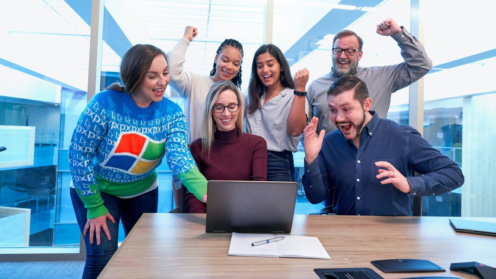 men and women sitting and standing by the table looking happy while staring at laptop