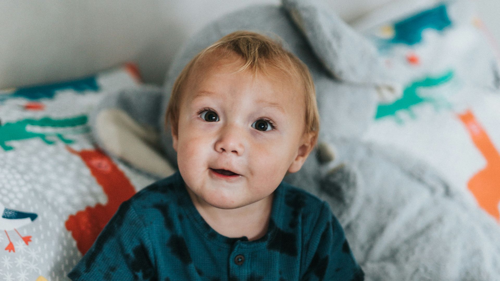 child in blue and red button up shirt sitting on bed