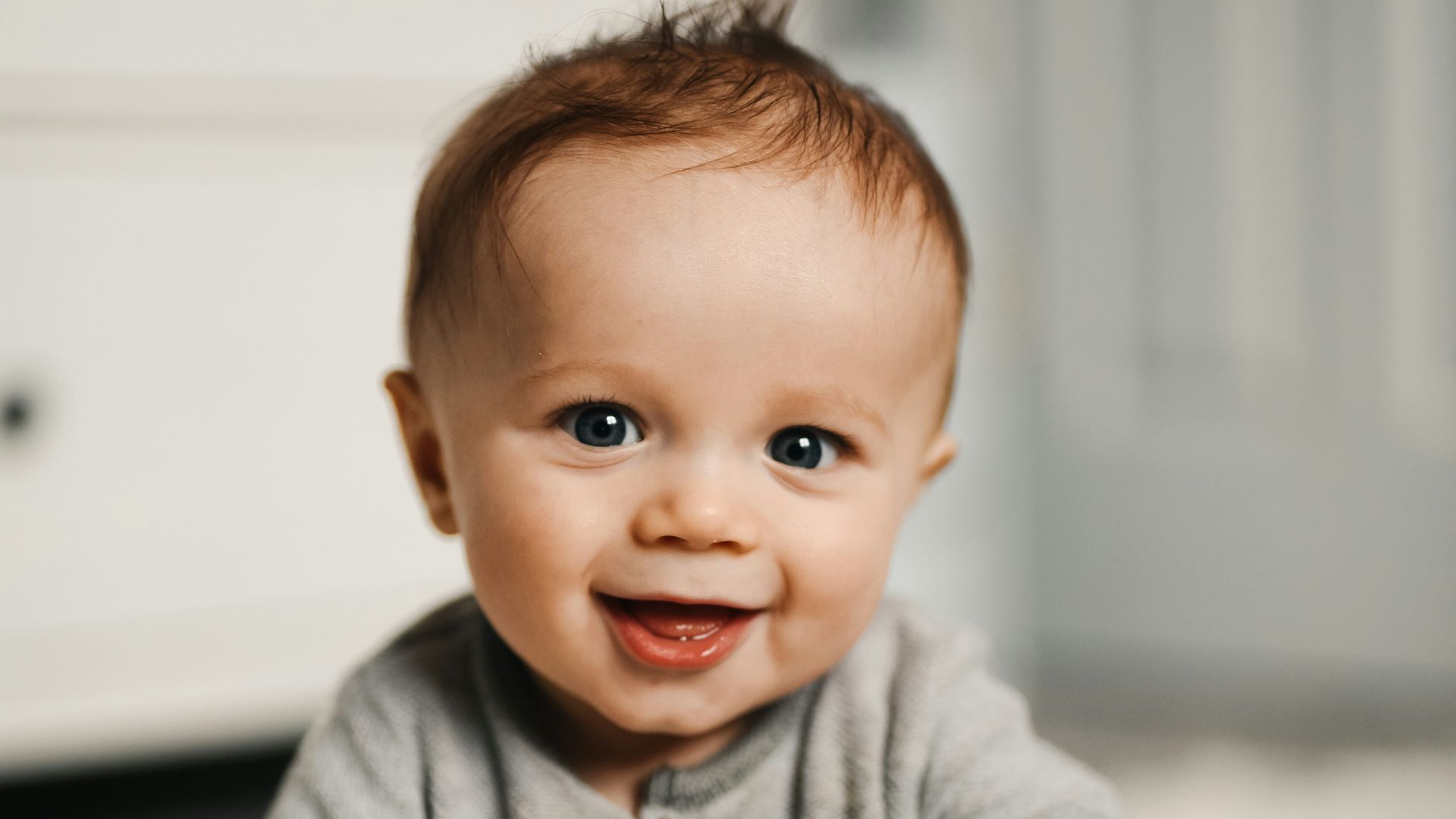 baby in gray sweater lying on white textile