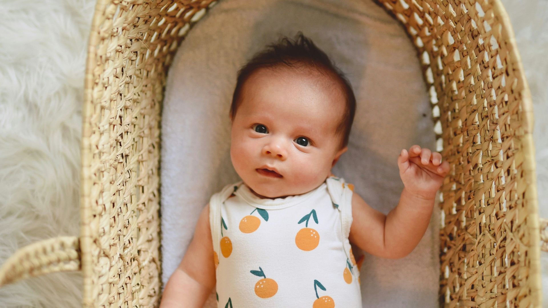 baby in white and green polka dot onesie lying on brown wicker basket