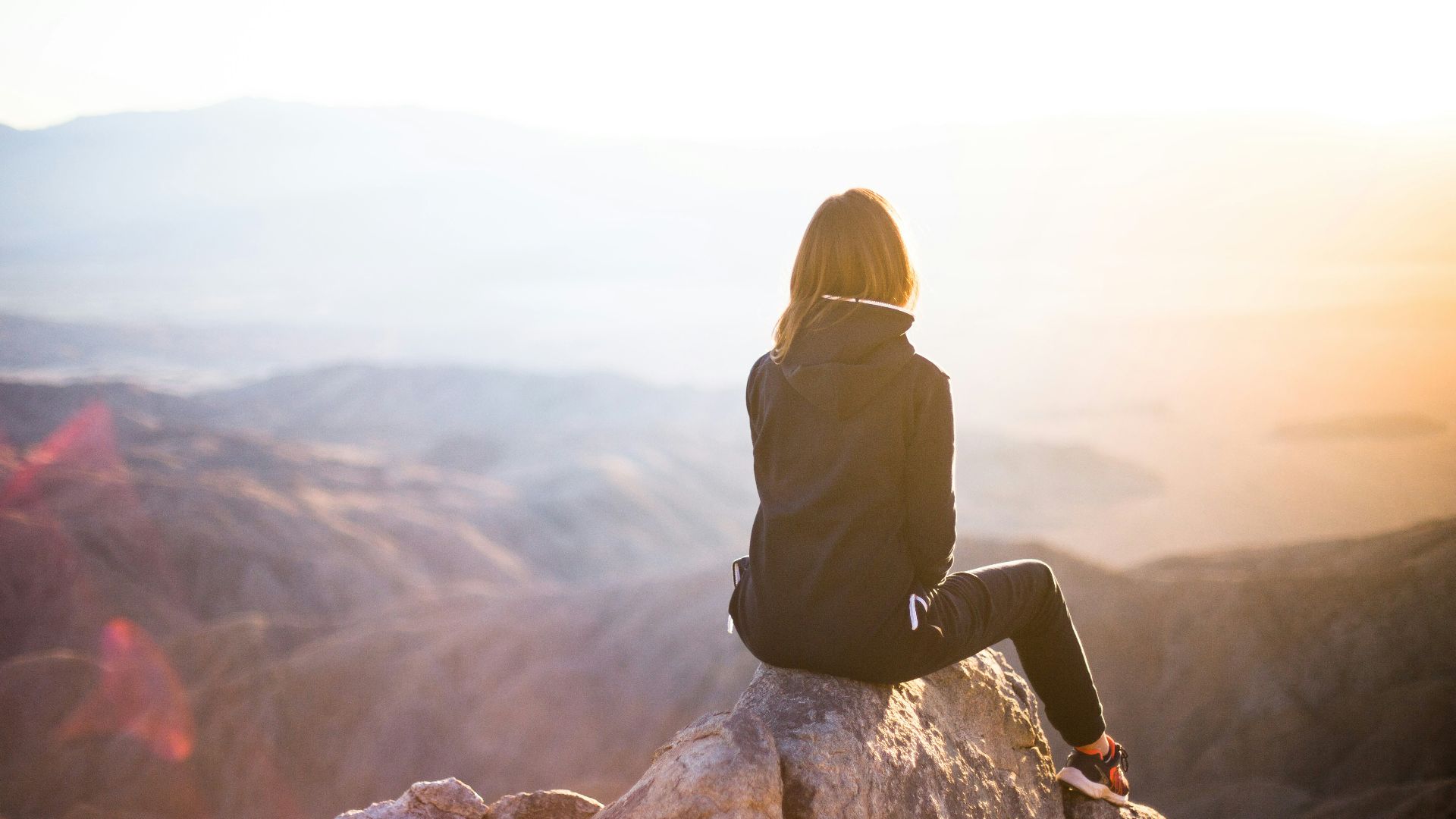 person sitting on top of gray rock overlooking mountain during daytime