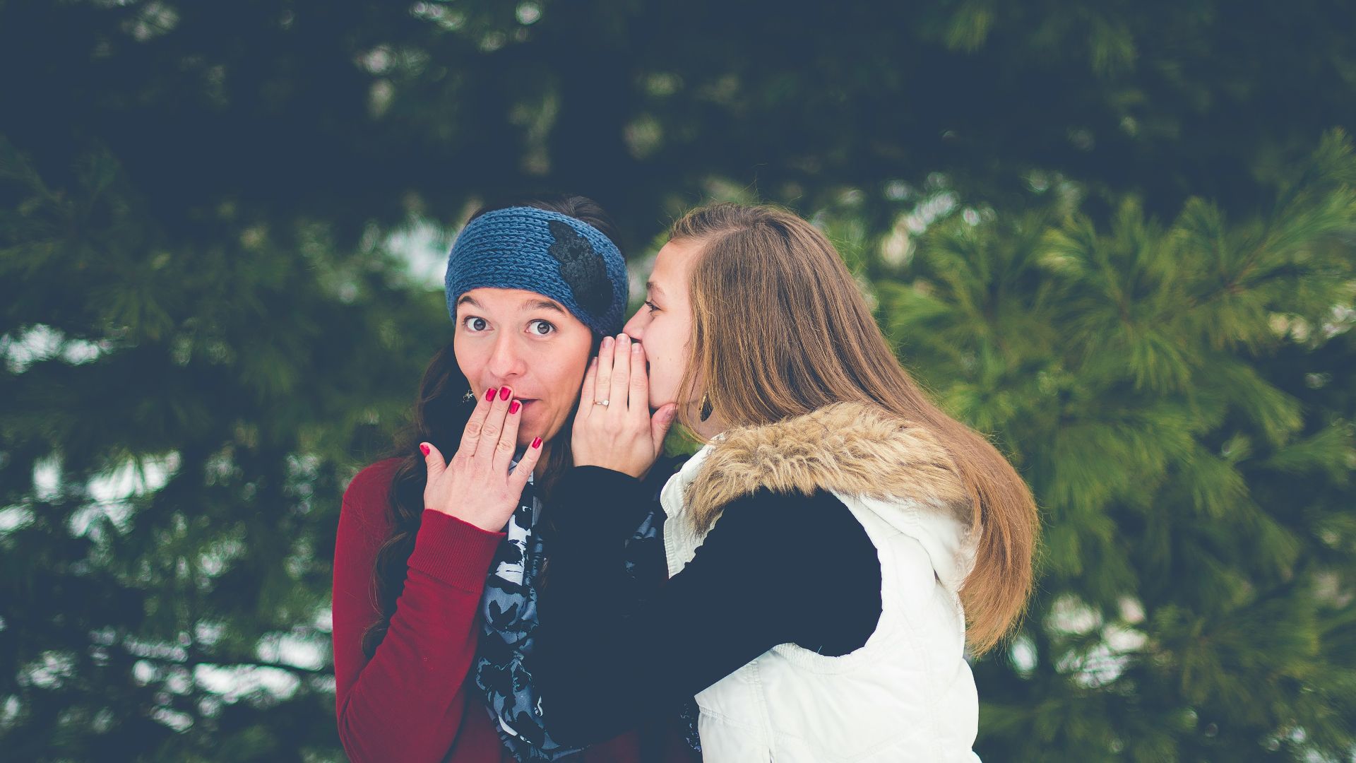 woman whispering on woman's ear while hands on lips