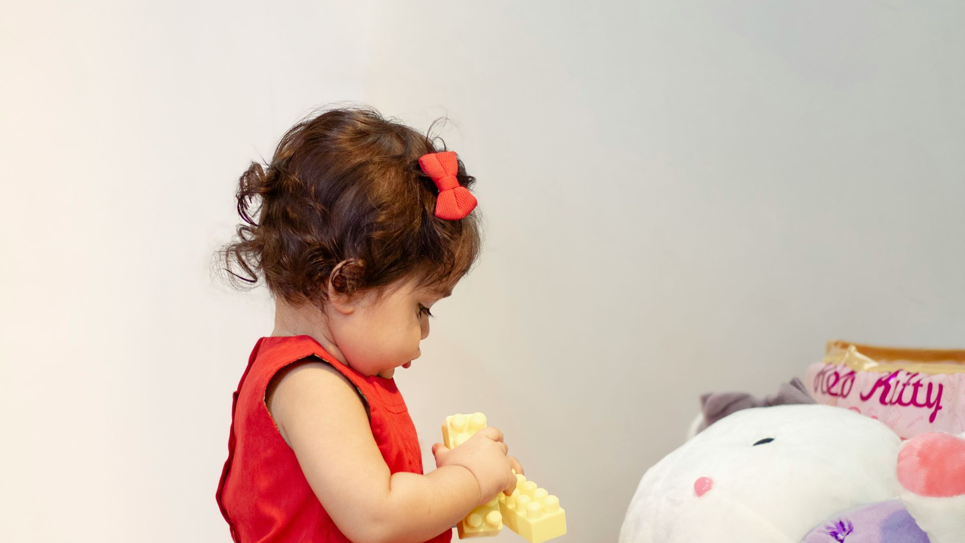 a little girl in a red dress playing with a stuffed animal