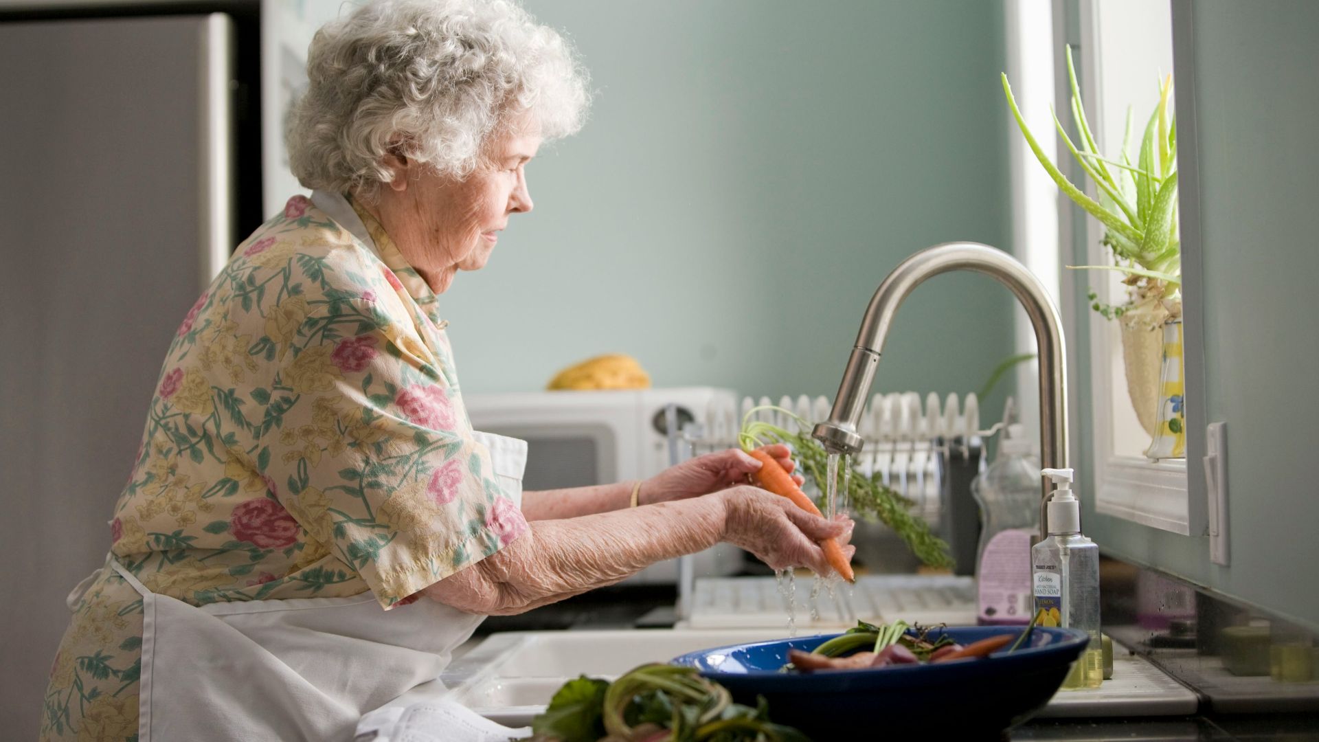 woman wearing yellow and pink floral dress wahing carrots
