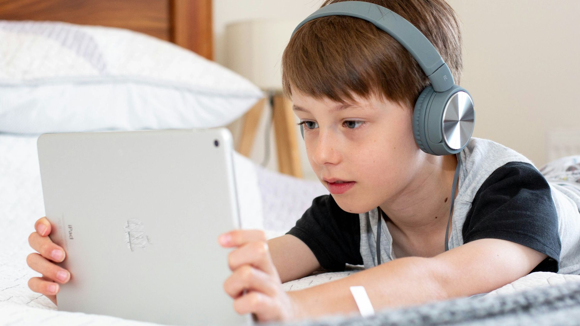 boy in blue shirt wearing headphones lying on bed