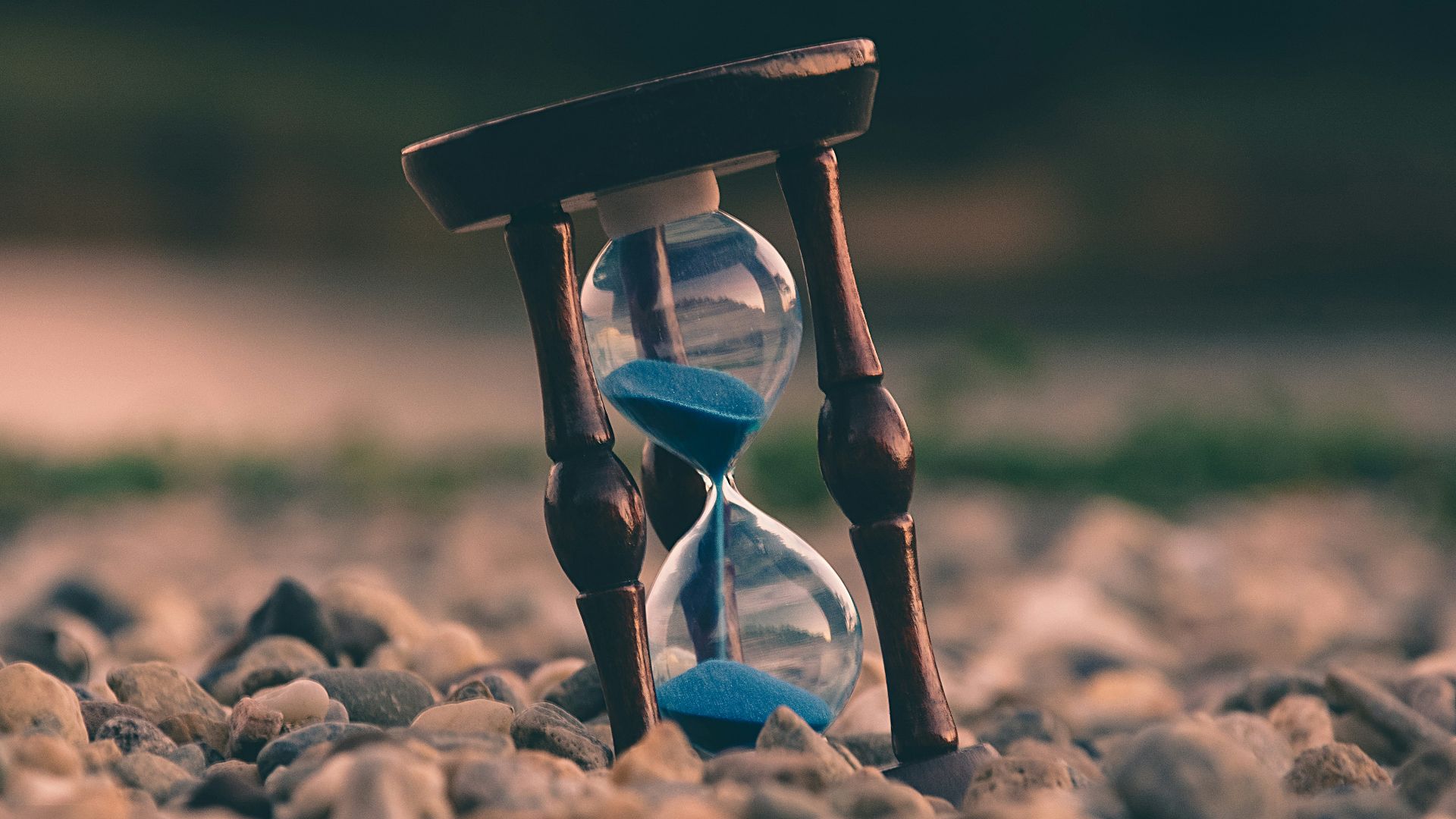selective focus photo of brown and blue hourglass on stones