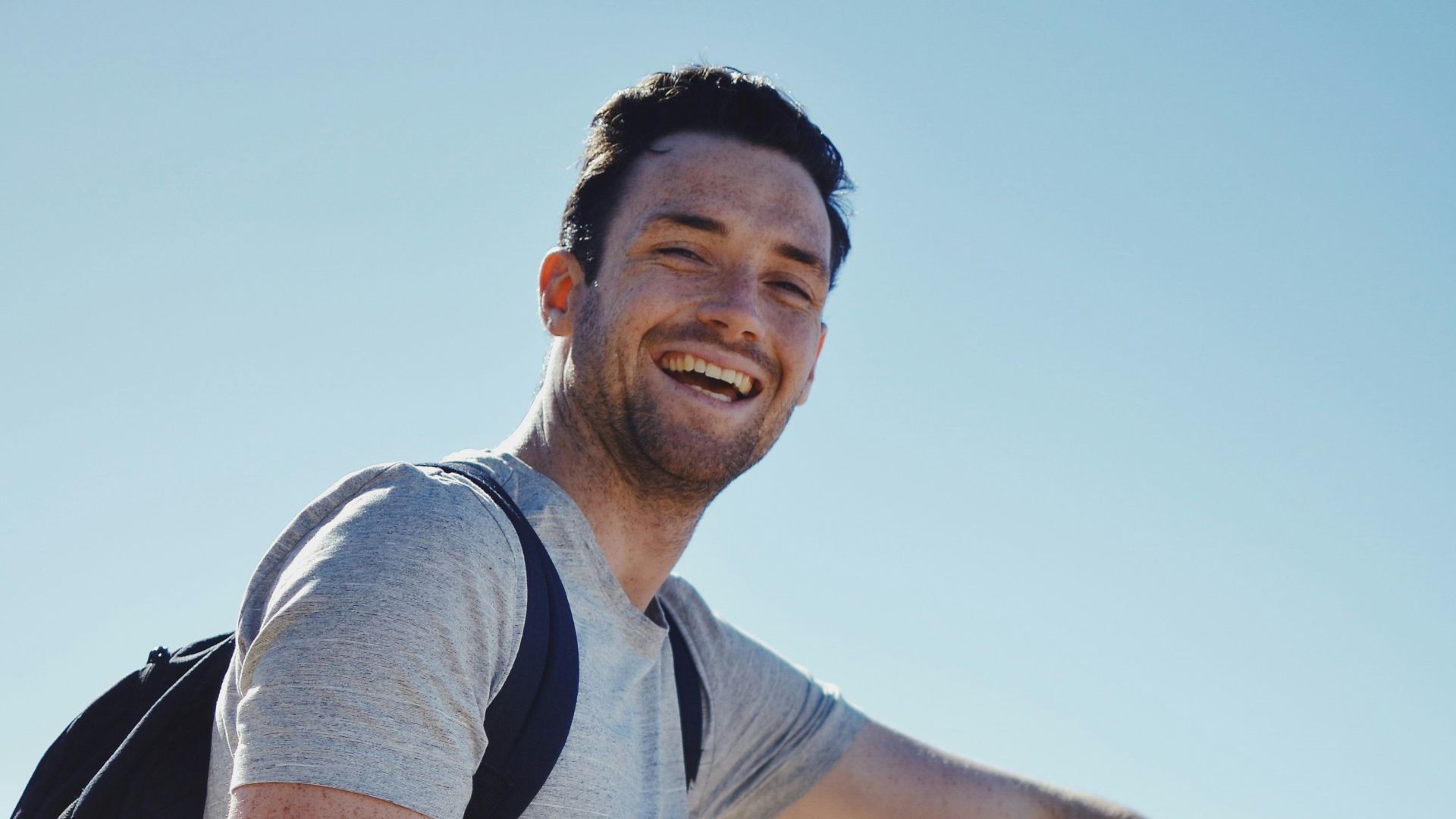 smiling man sitting on gray rock at daytime