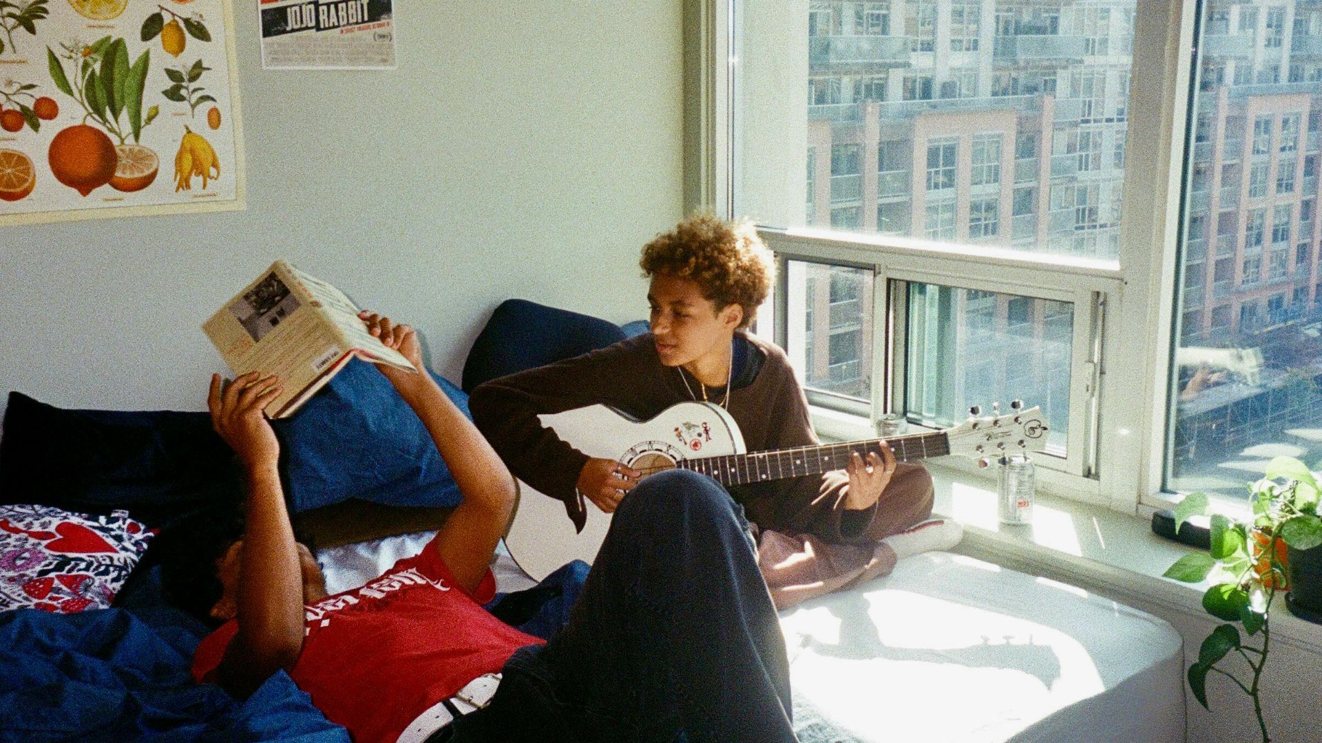a young man sitting on a bed reading a book