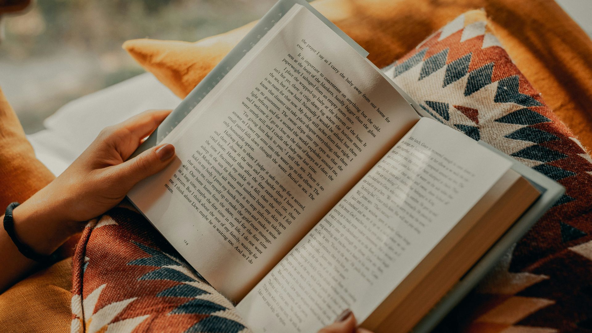 person reading book on brown and beige textile