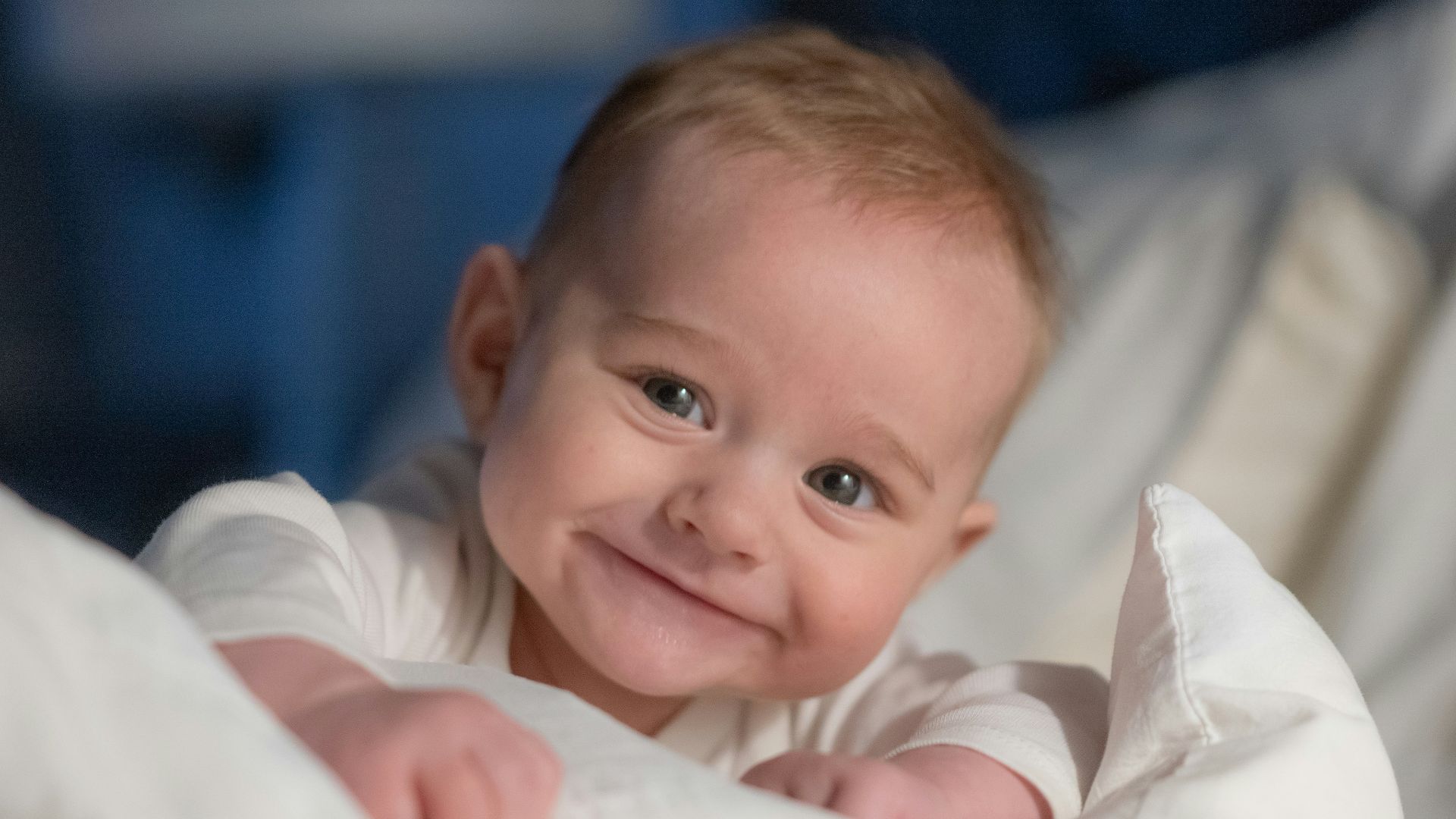 A smiling baby wrapped in a blanket on a bed