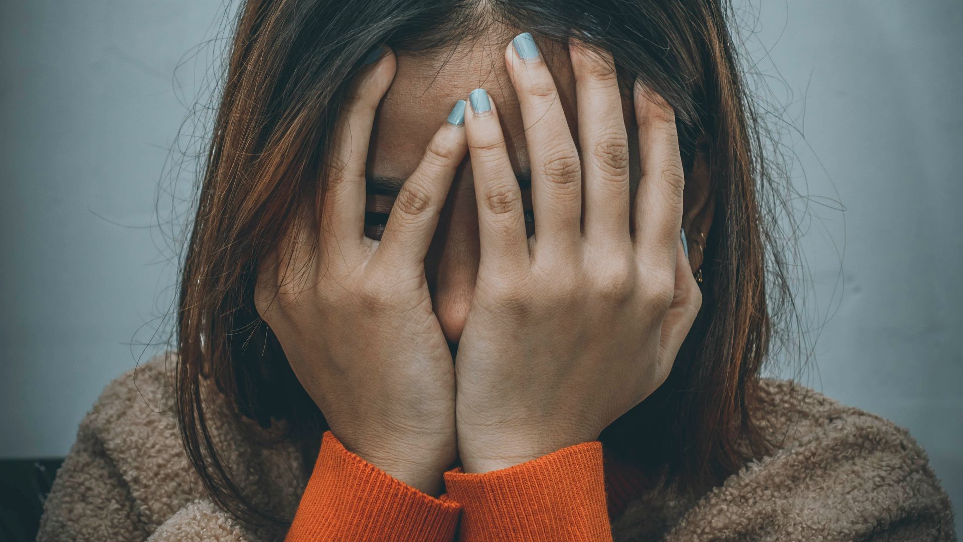 woman in brown sweater covering her face with her hand