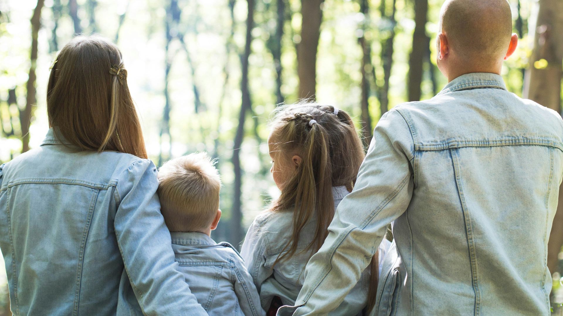 man and woman holding hands together with boy and girl looking at green trees during day