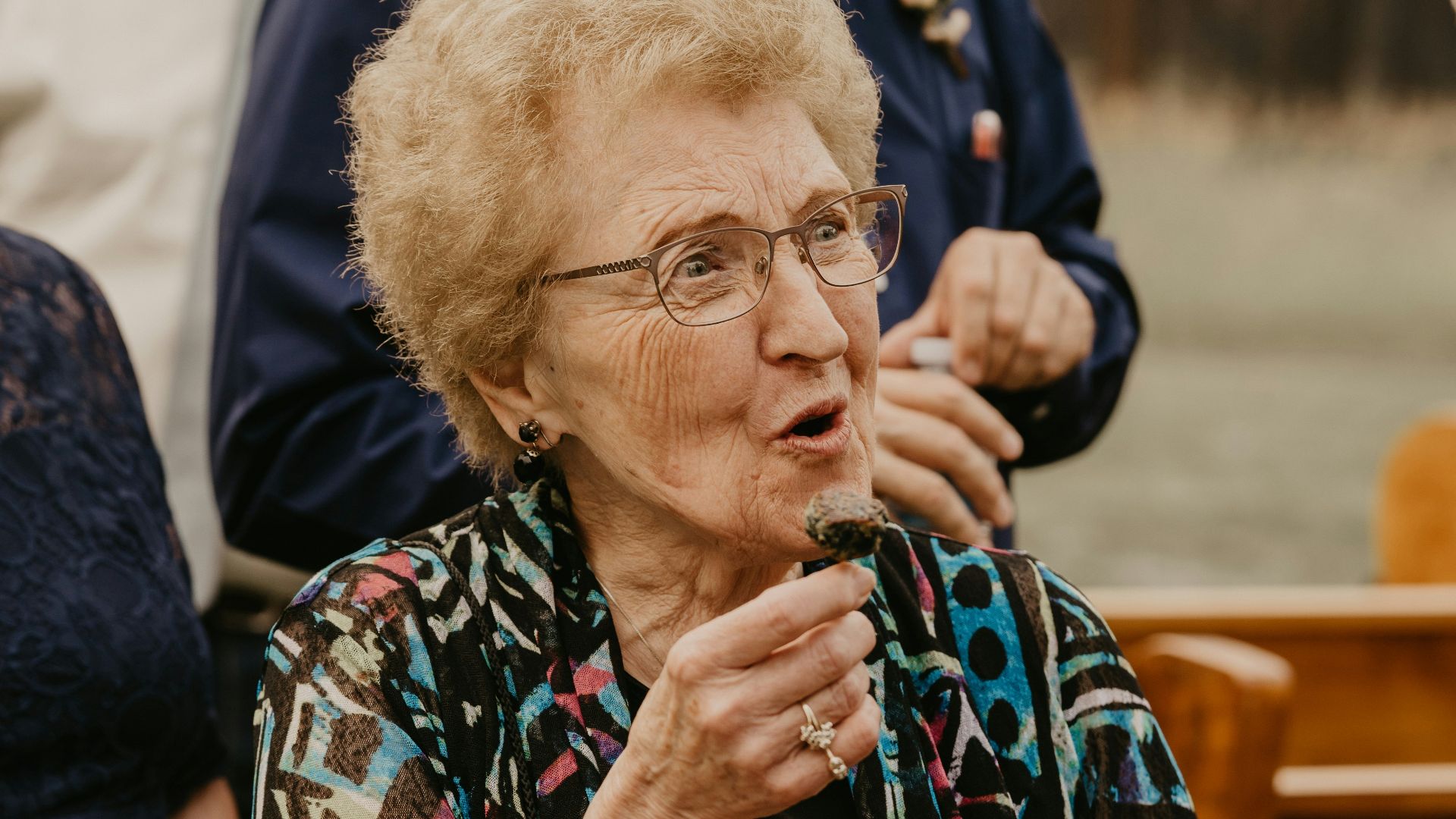 an older woman holding a tray of cupcakes