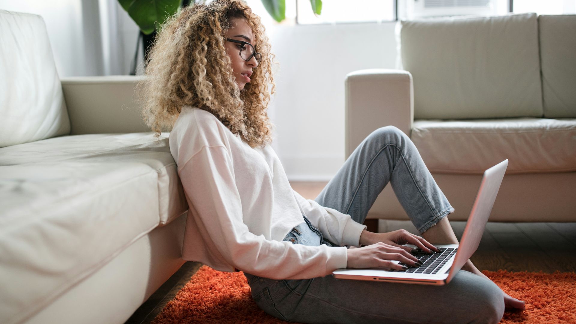 woman sitting on floor and leaning on couch using laptop