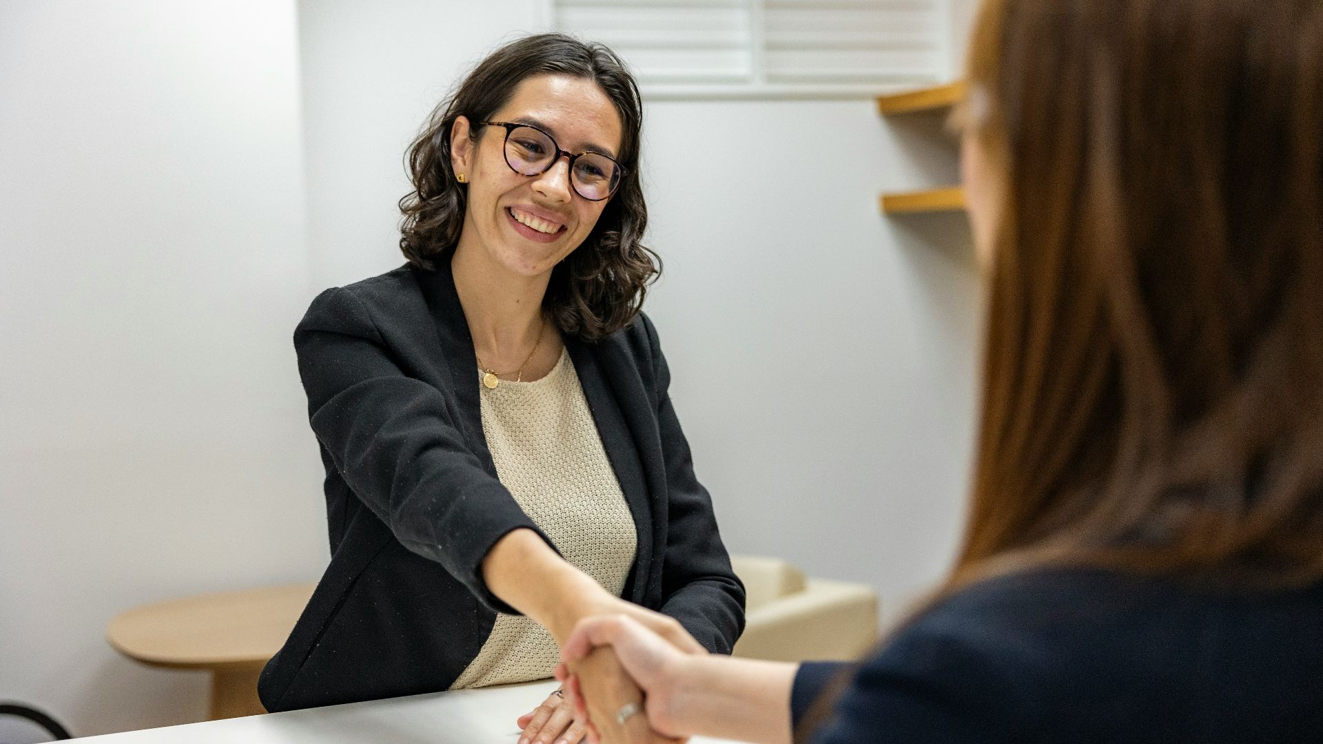 a woman shaking hands with another woman sitting at a table