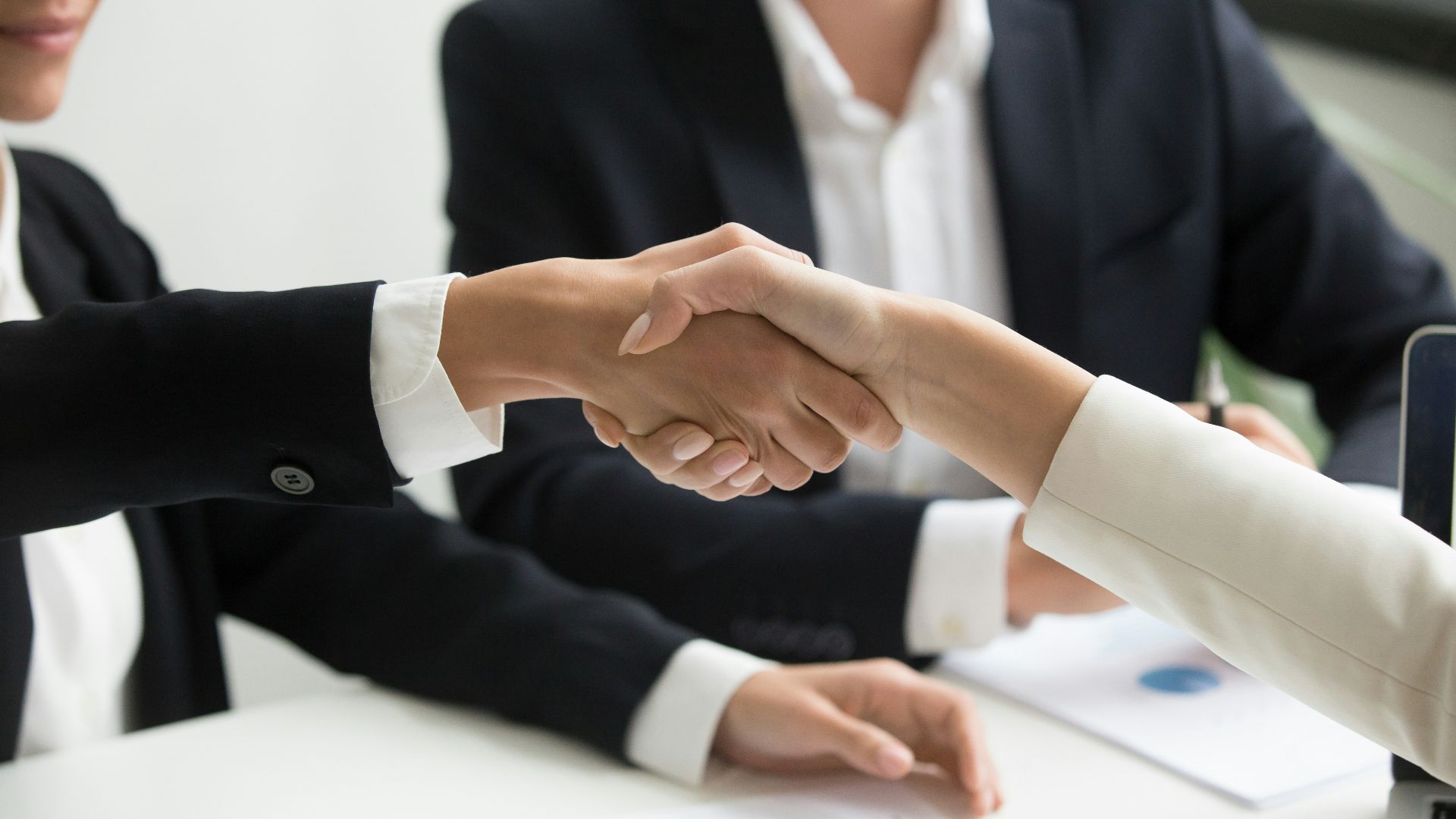 two people shaking hands in front of a laptop