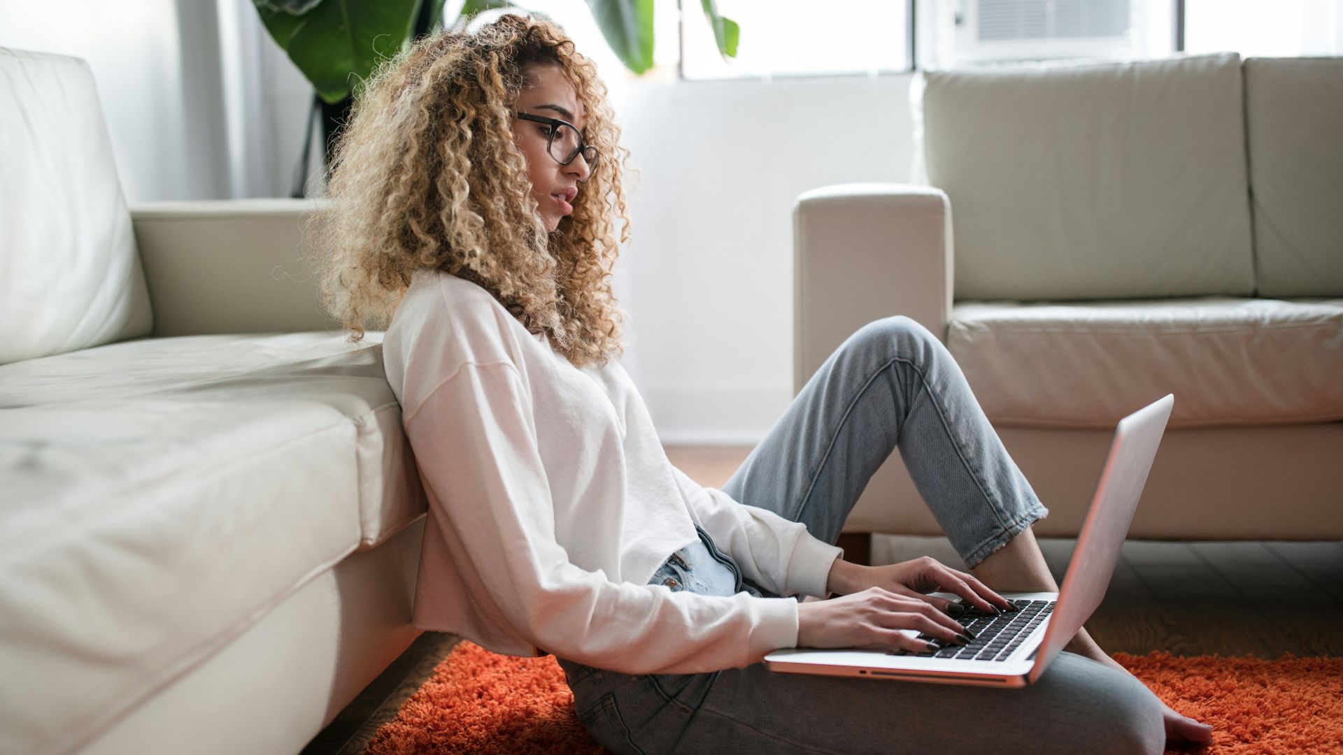 woman sitting on floor and leaning on couch using laptop