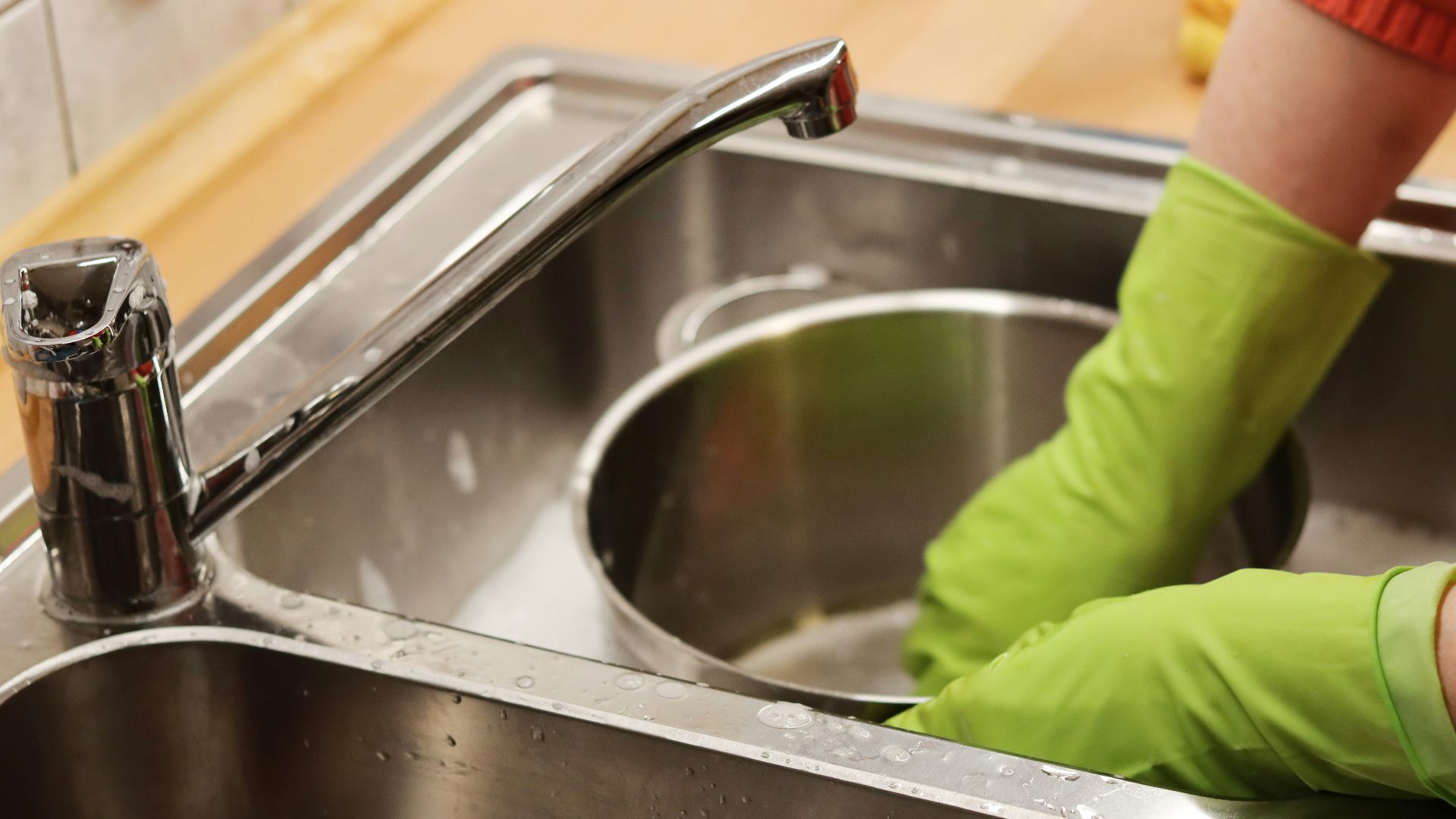 person in green long sleeve shirt washing stainless steel sink
