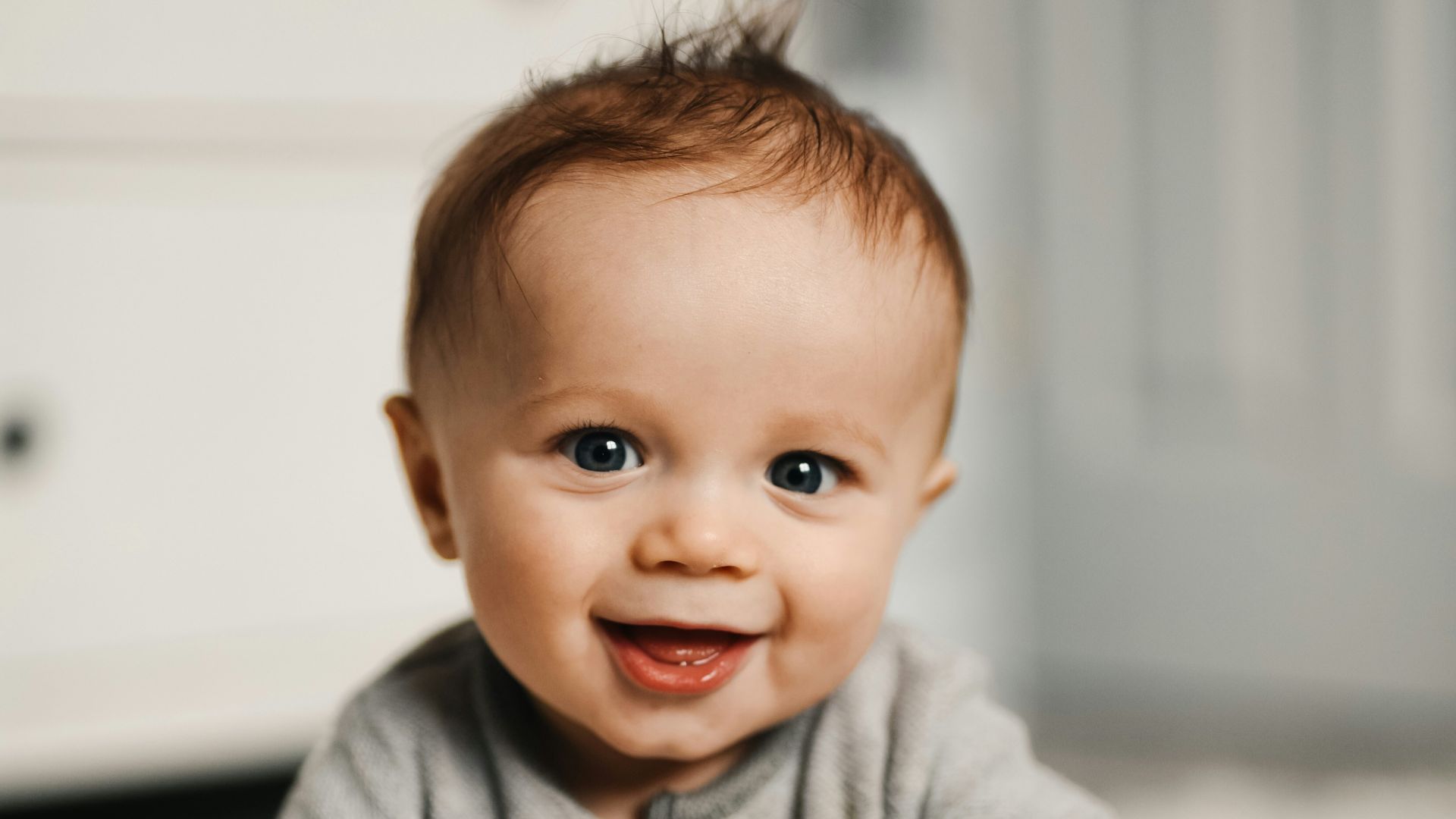 baby in gray sweater lying on white textile