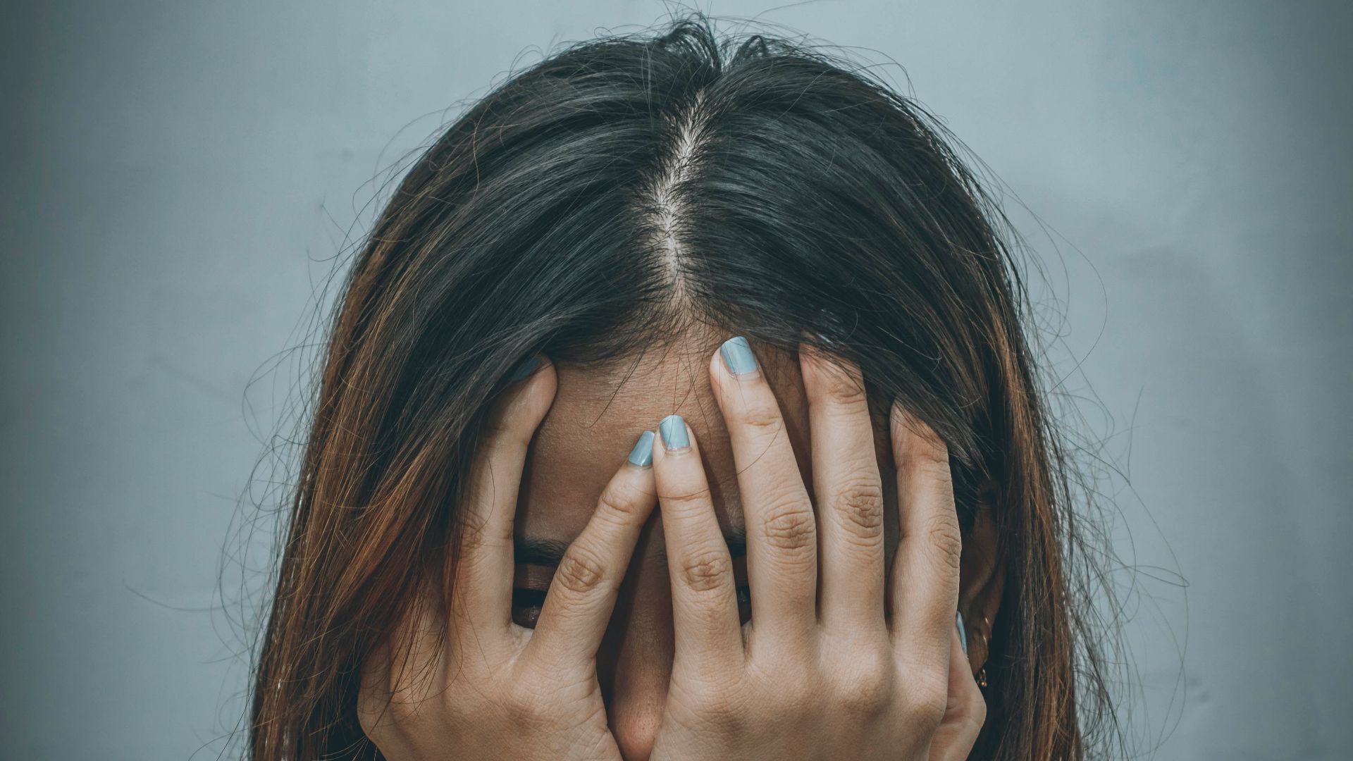 woman in brown sweater covering her face with her hand