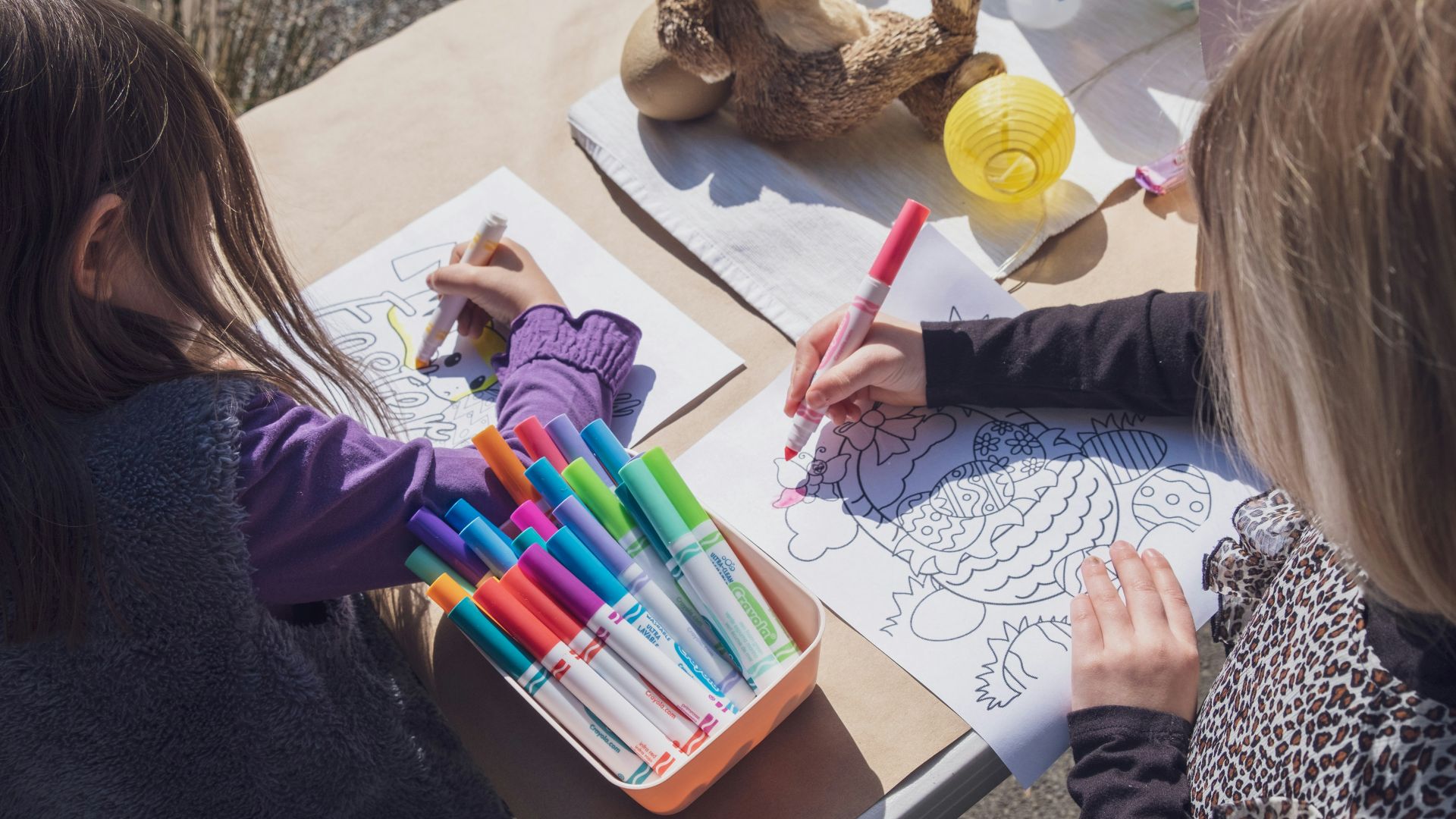 two young girls sitting at a table with markers and crayons