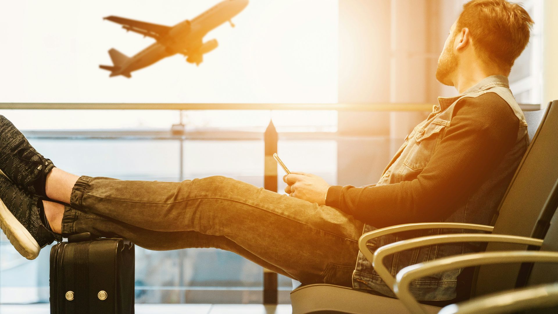 man sitting on gang chair with feet on luggage looking at airplane