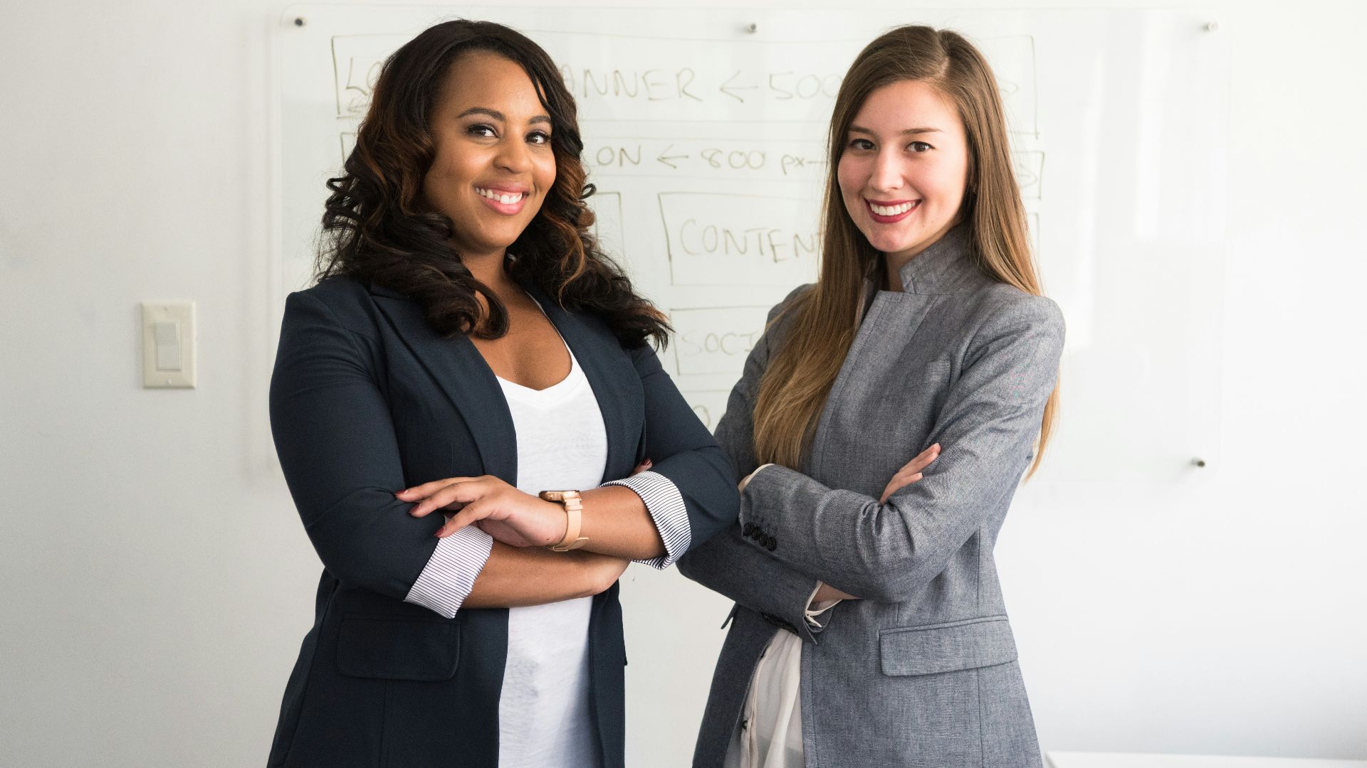 two women in suits standing beside wall