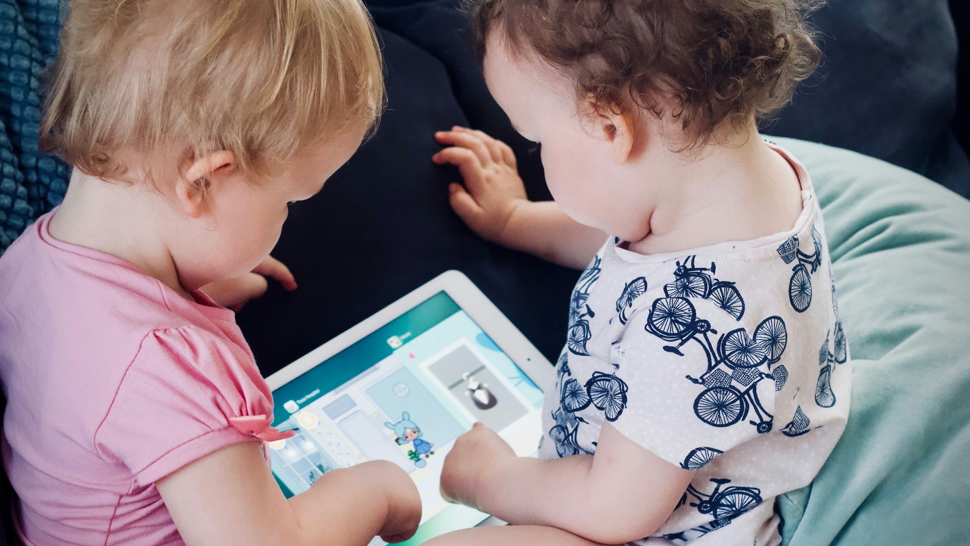 two toddlers sitting on sofa while using tablet computer
