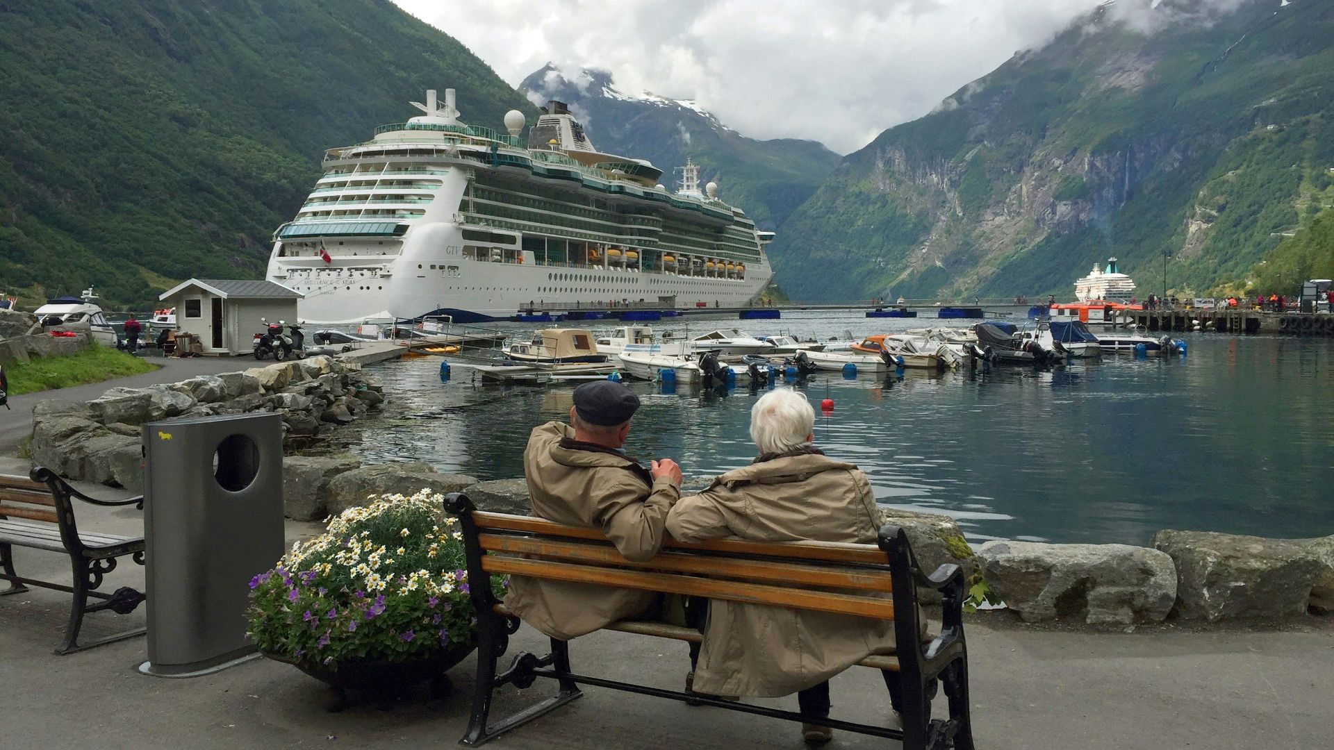 woman in brown coat sitting on brown wooden bench near white cruise ship during daytime