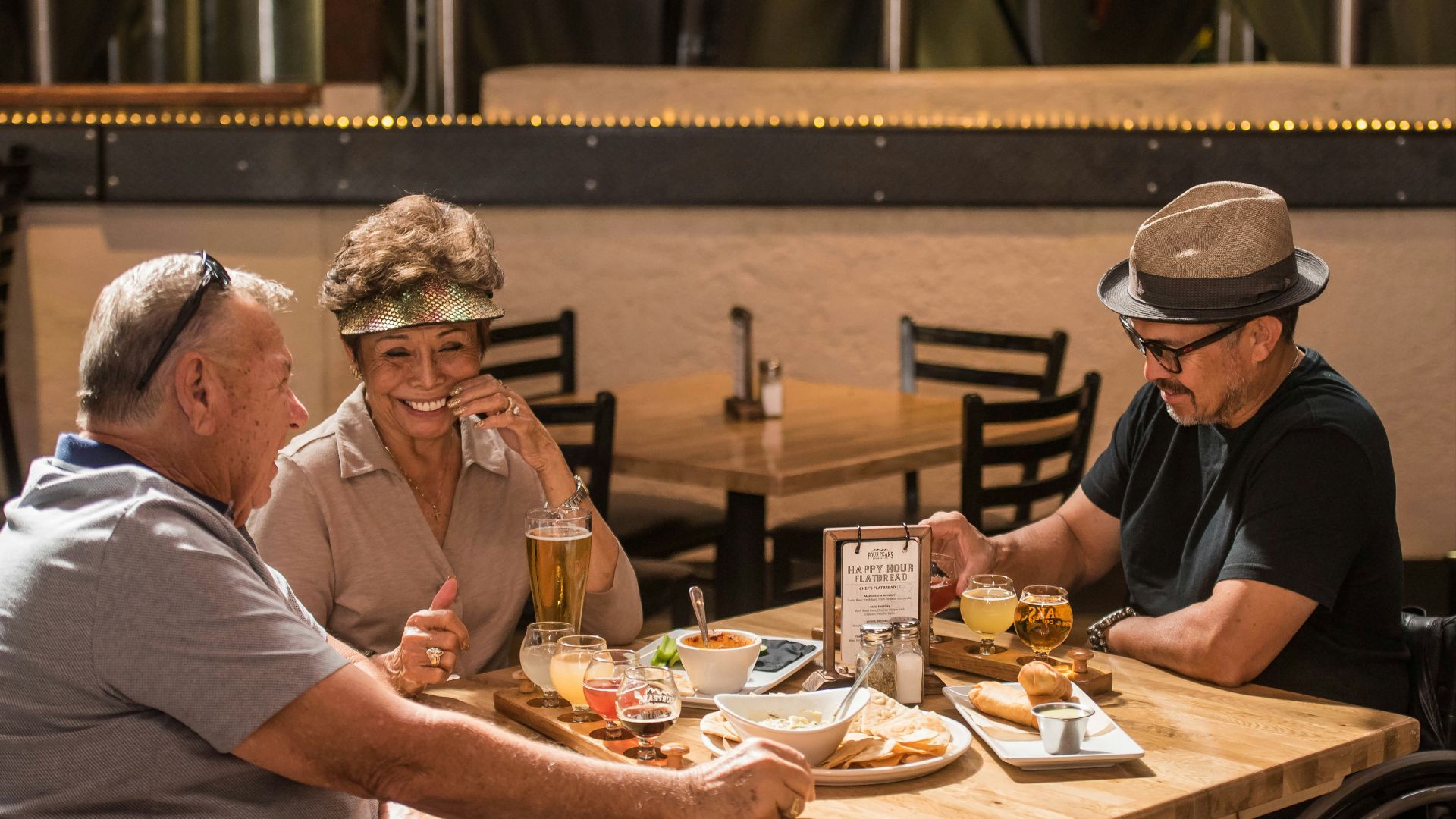 three smiling people sitting beside table with plate of foods and drinks