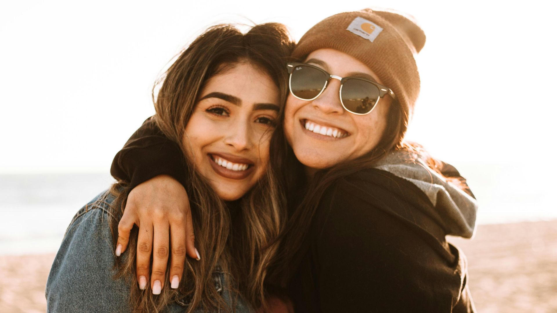 woman hugging other woman while smiling at beach