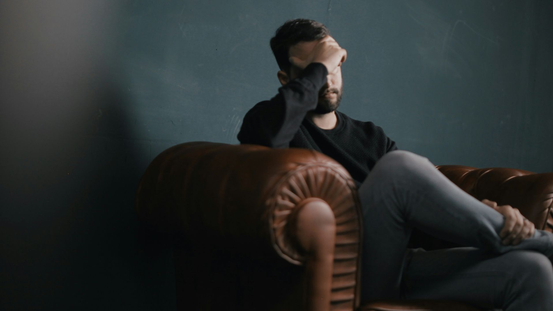 a man holds his head while sitting on a sofa