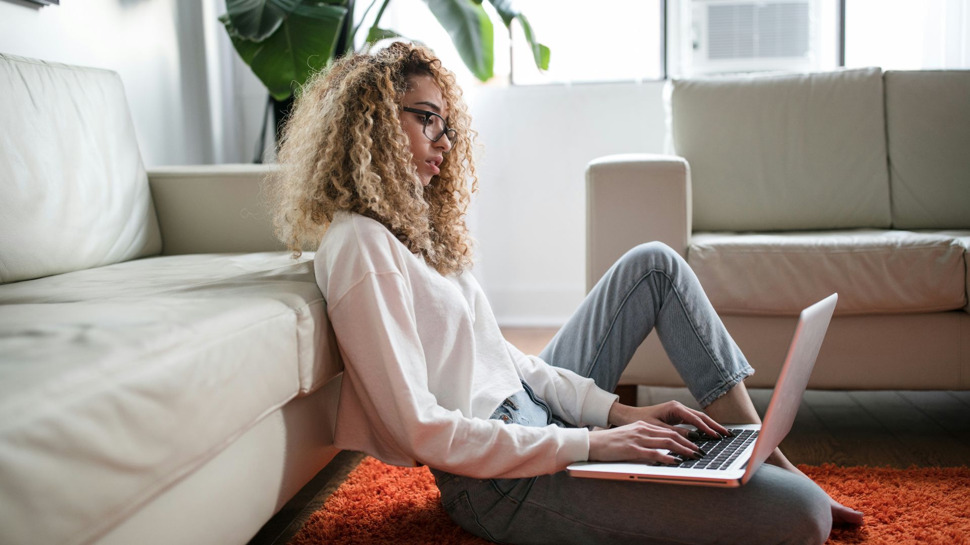 woman sitting on floor and leaning on couch using laptop