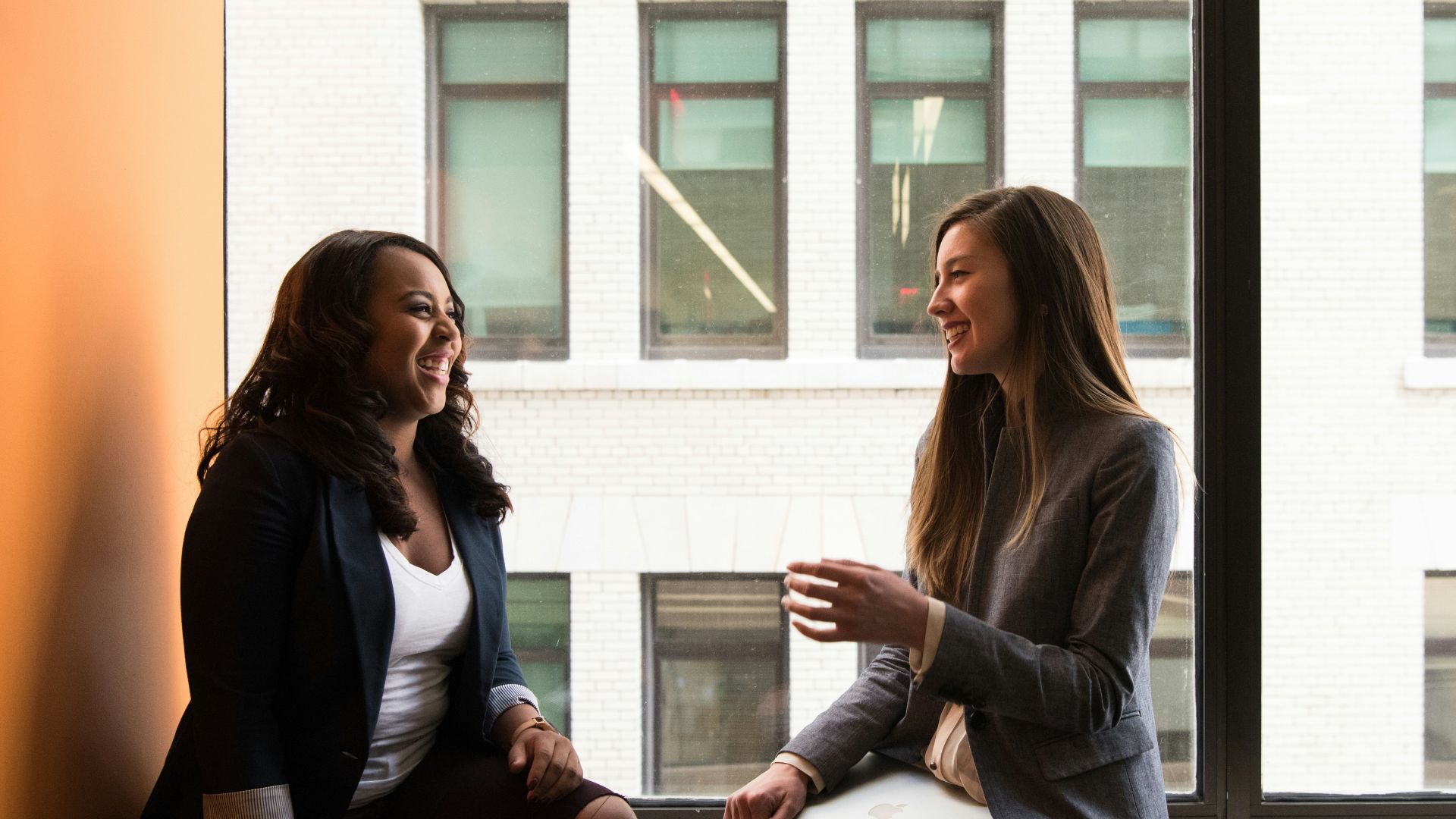 two woman sitting by the window laughing